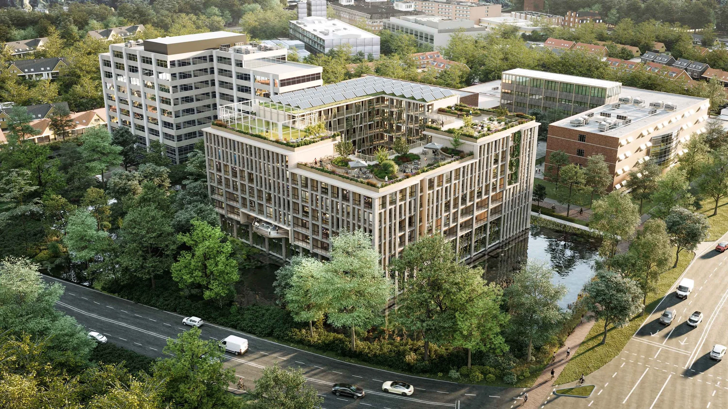 Aerial view of a modern multi-story building with rooftop gardens and solar panels, surrounded by trees and streets with cars and cyclists.