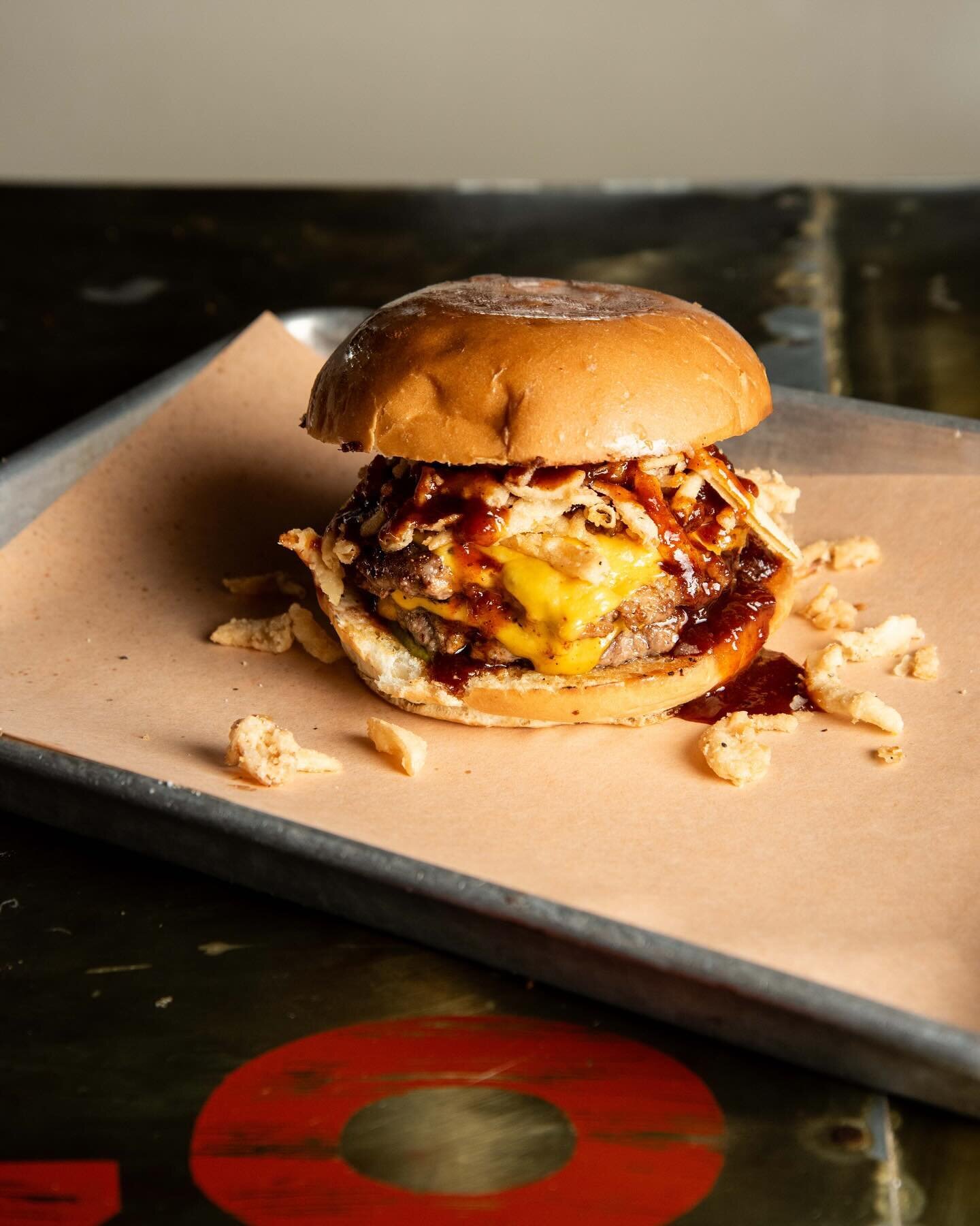 Thank you @grubfreaks for capturing our Smokehouse Burger! We blend our own meat, top it with American cheese, bbq sauce, smoked tallow mayo, pickles, and crispy fried onions, and serve it on a bun made at our bakery, @tgmbread. Come + get it! #woods