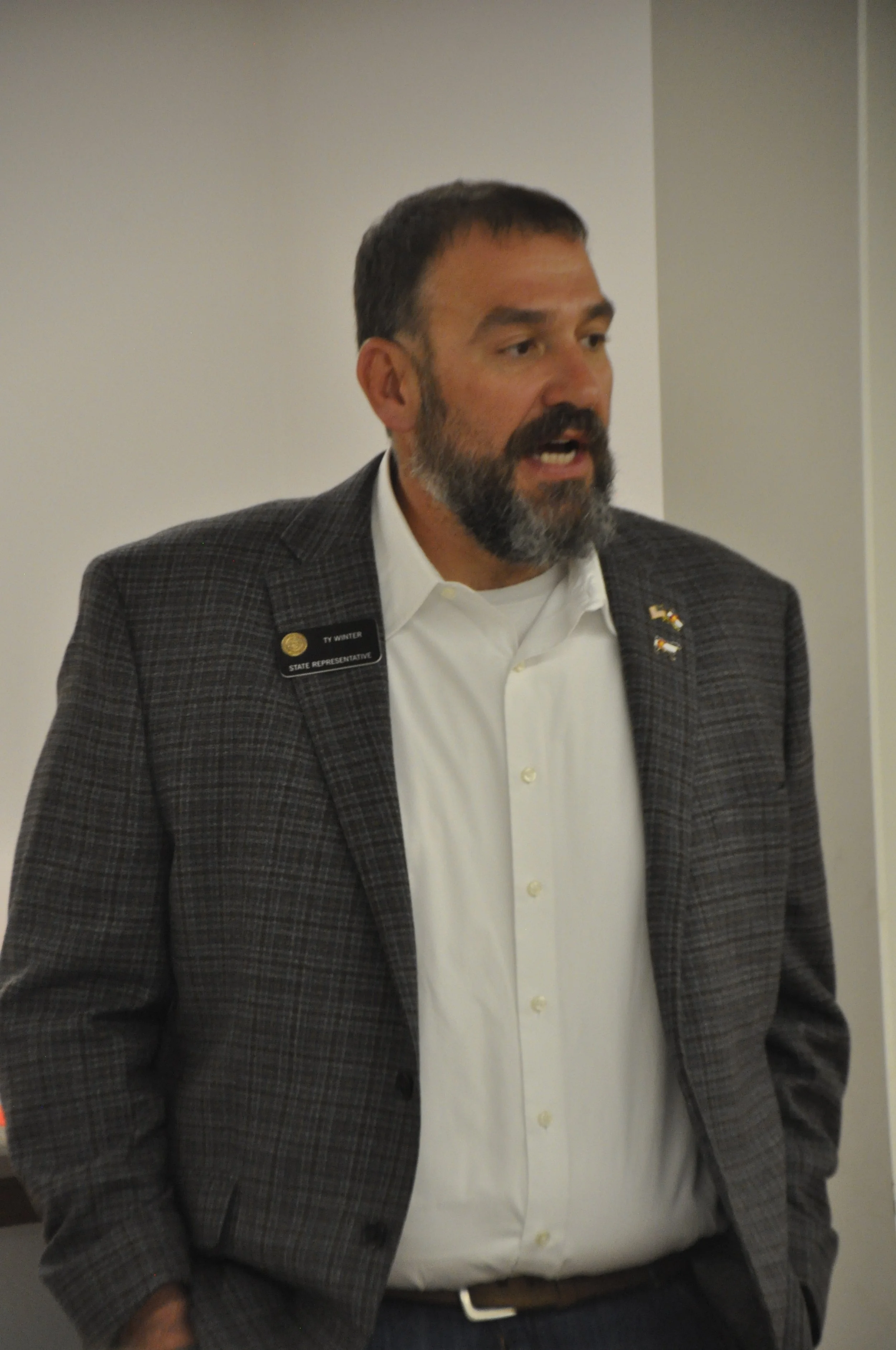 A man in a plaid suit jacket and white shirt speaking at an event.
