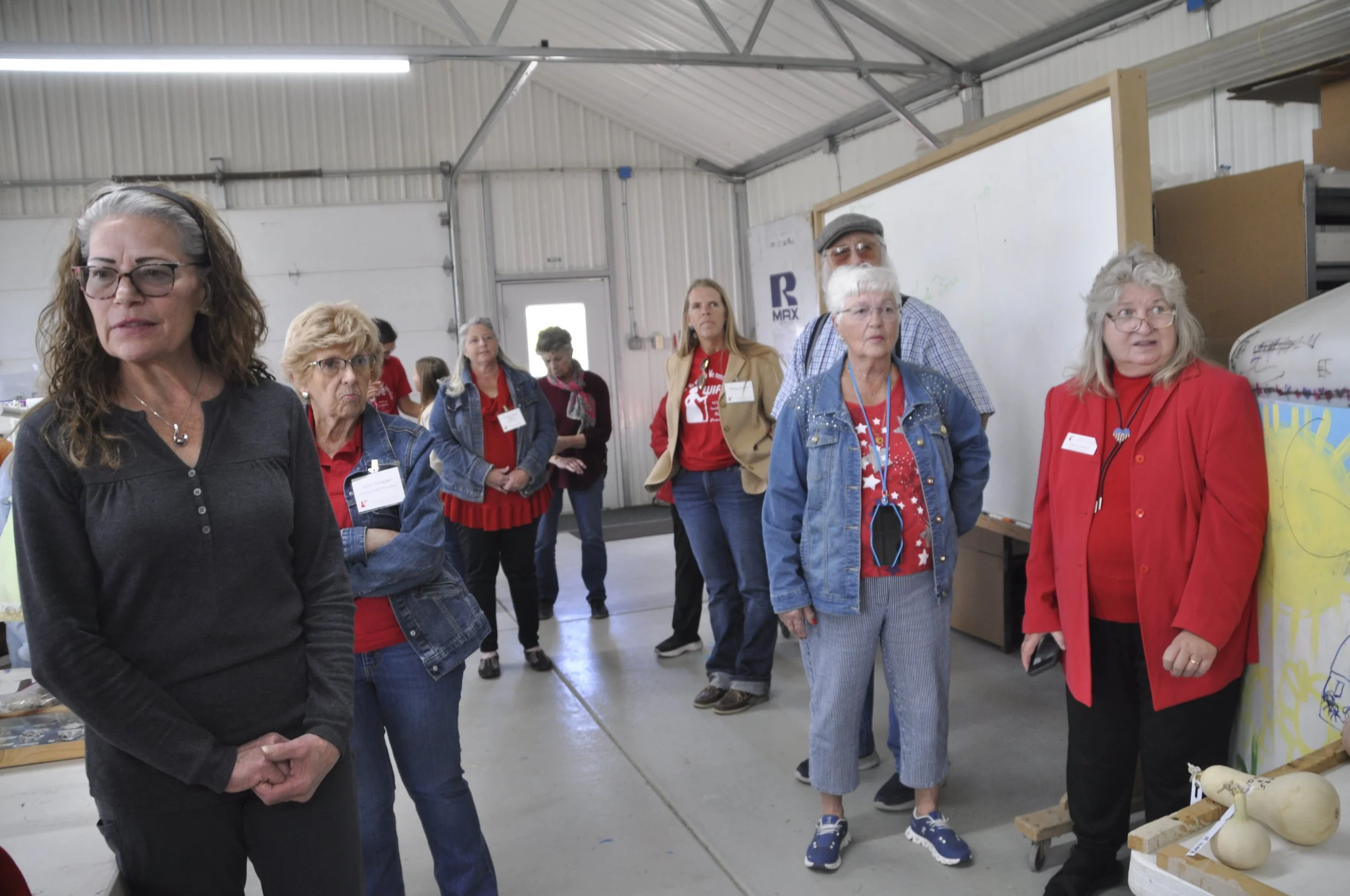 Group of people gathered indoors, looking at an exhibit or display, with some wearing name tags.