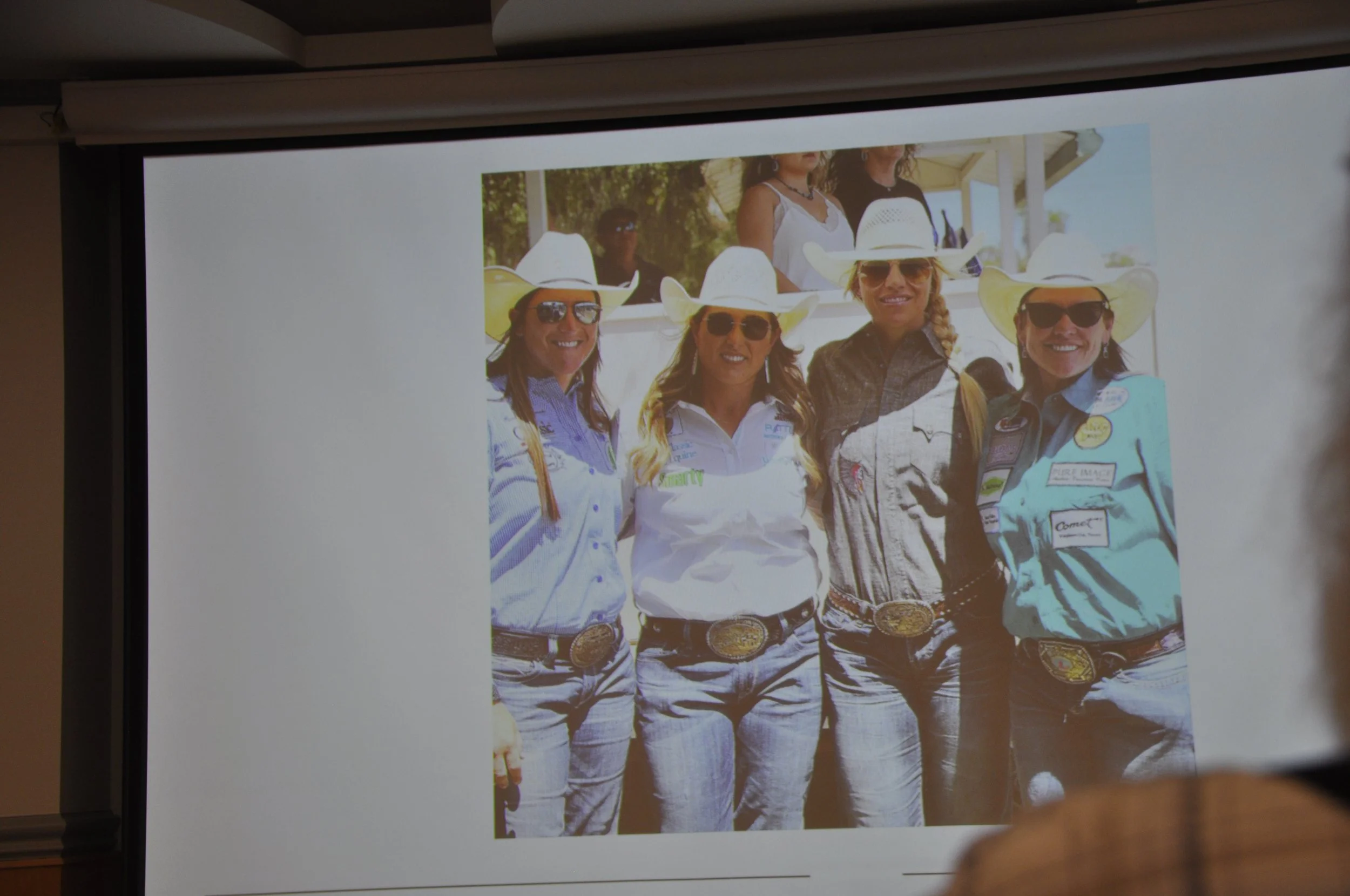 Photo of four women wearing cowboy hats, sunglasses, and western attire, standing outdoors.