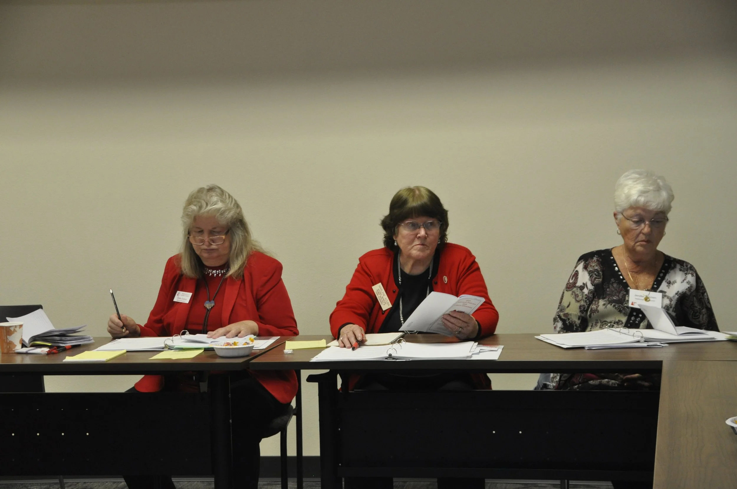 Three women sitting at a conference table reviewing papers and documents.