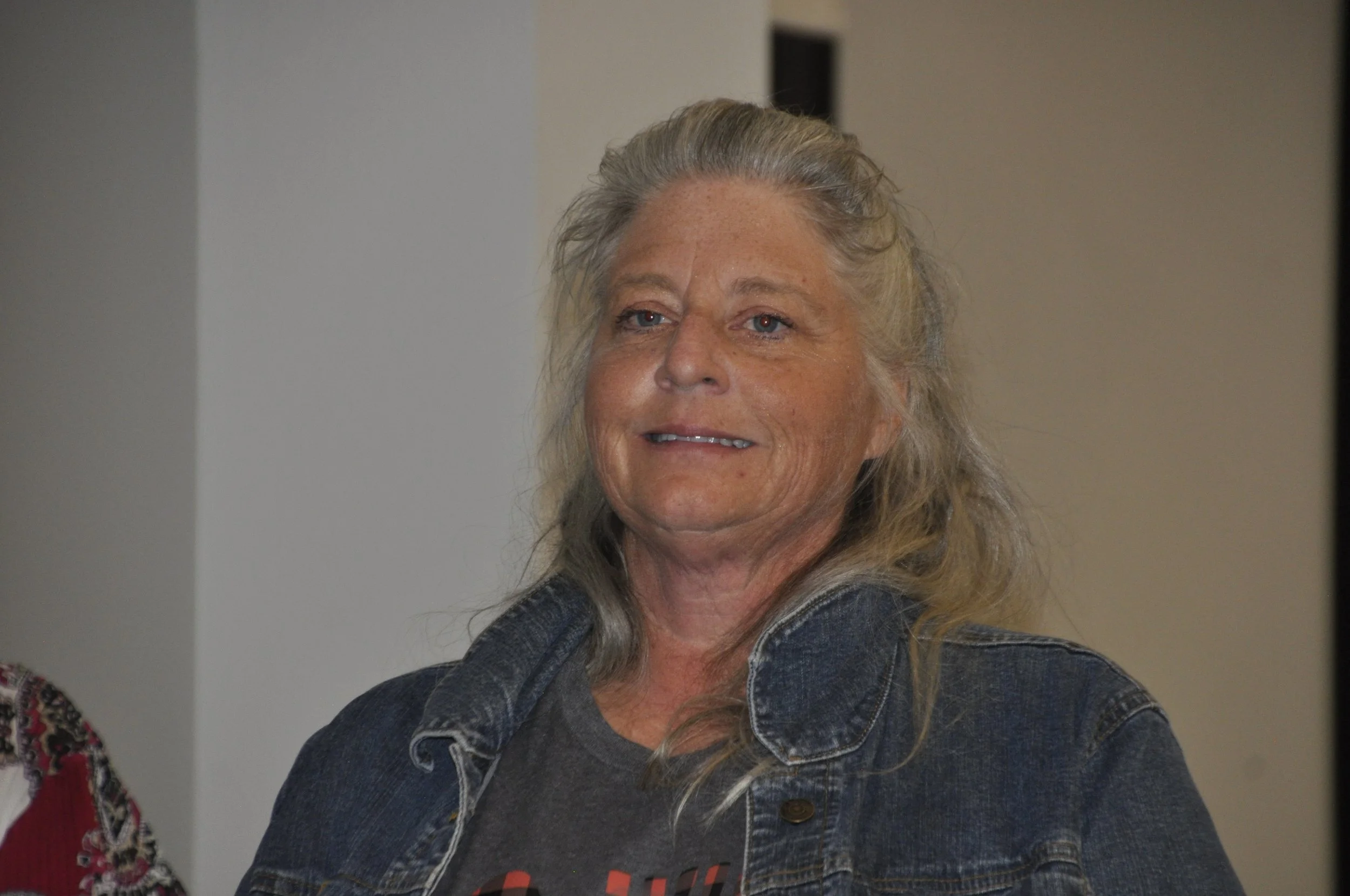 A smiling woman with long blonde hair wearing a denim jacket.