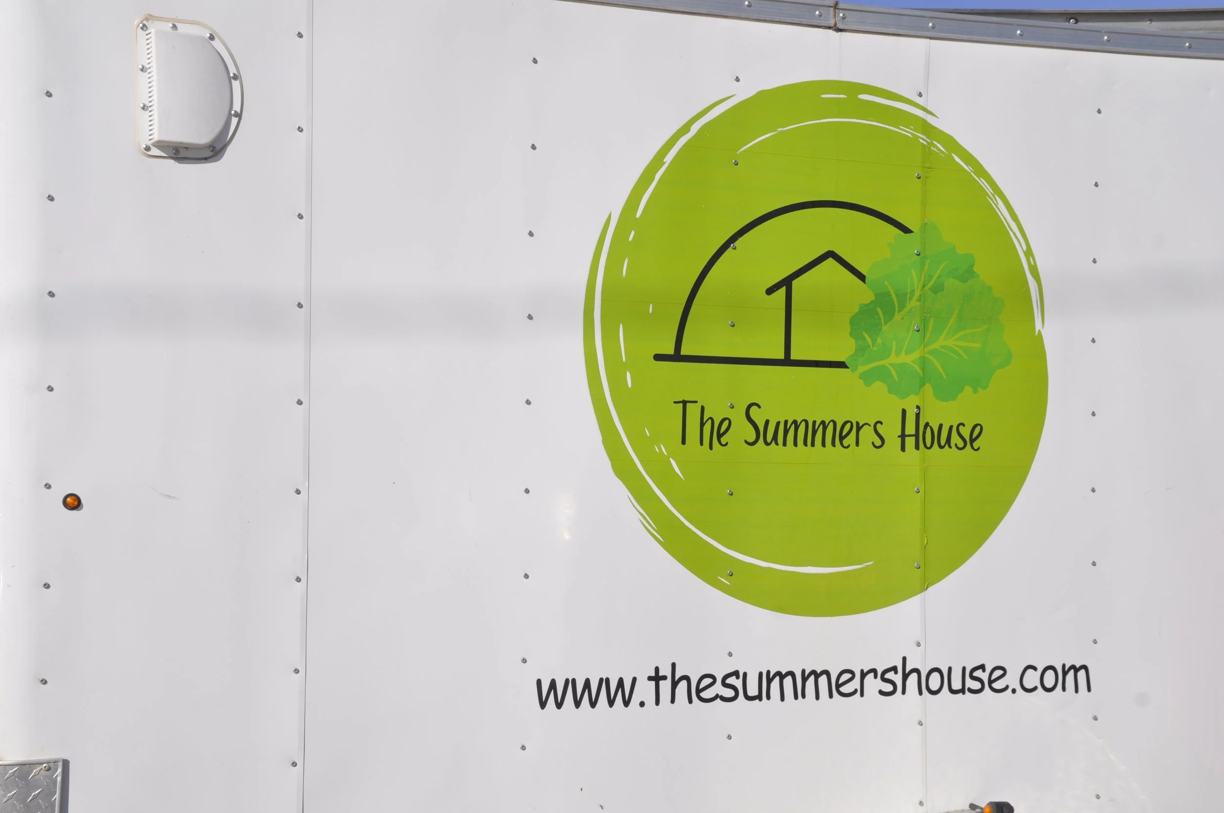 Sign with green circle logo featuring a house and leafy green plant, text 'The Summers House', and website 'www.thesummershouse.com' on a white background.