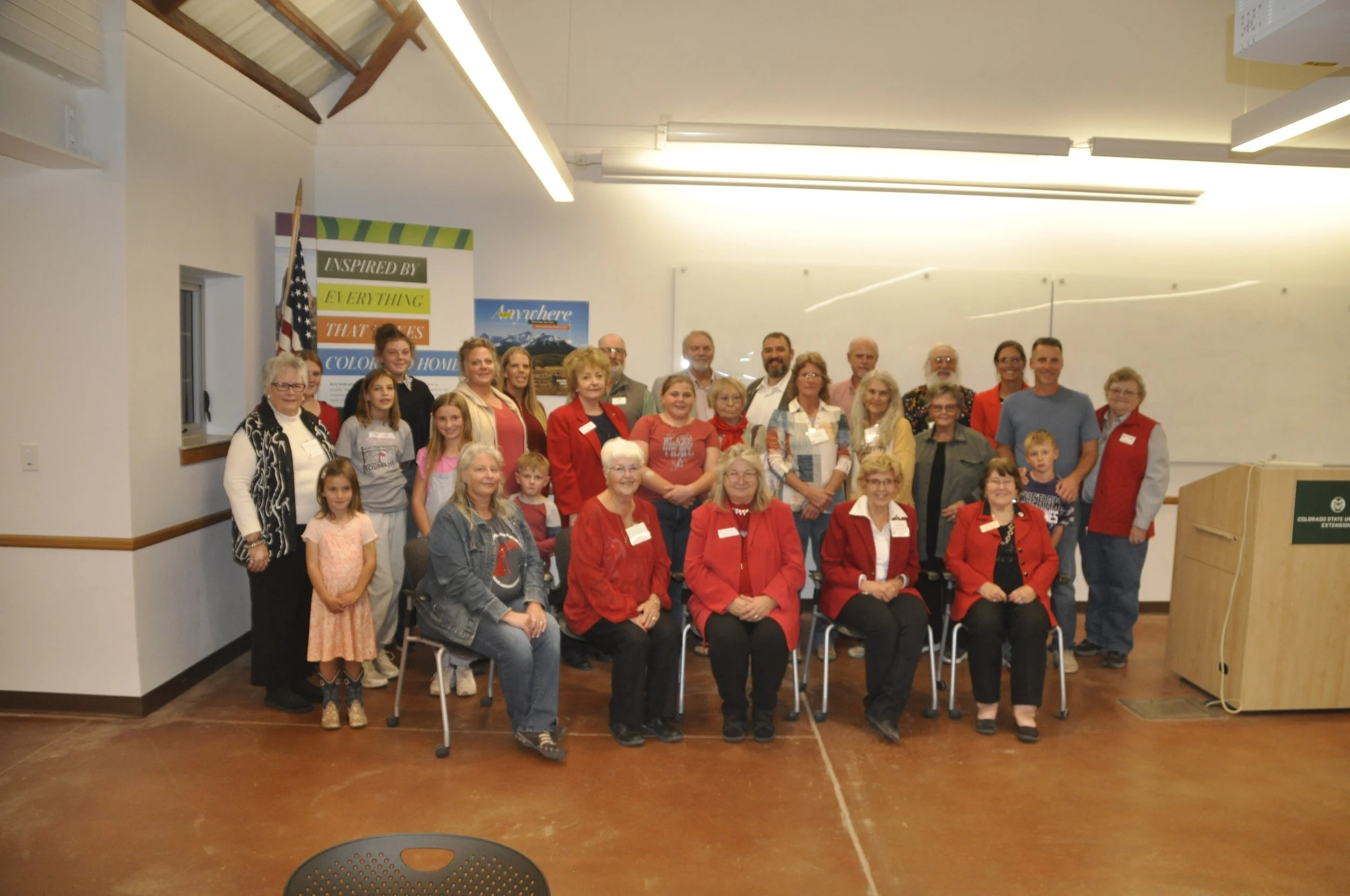 Group of diverse people gathered indoors, smiling for a group photo, with a colorful poster and American flag in the background.