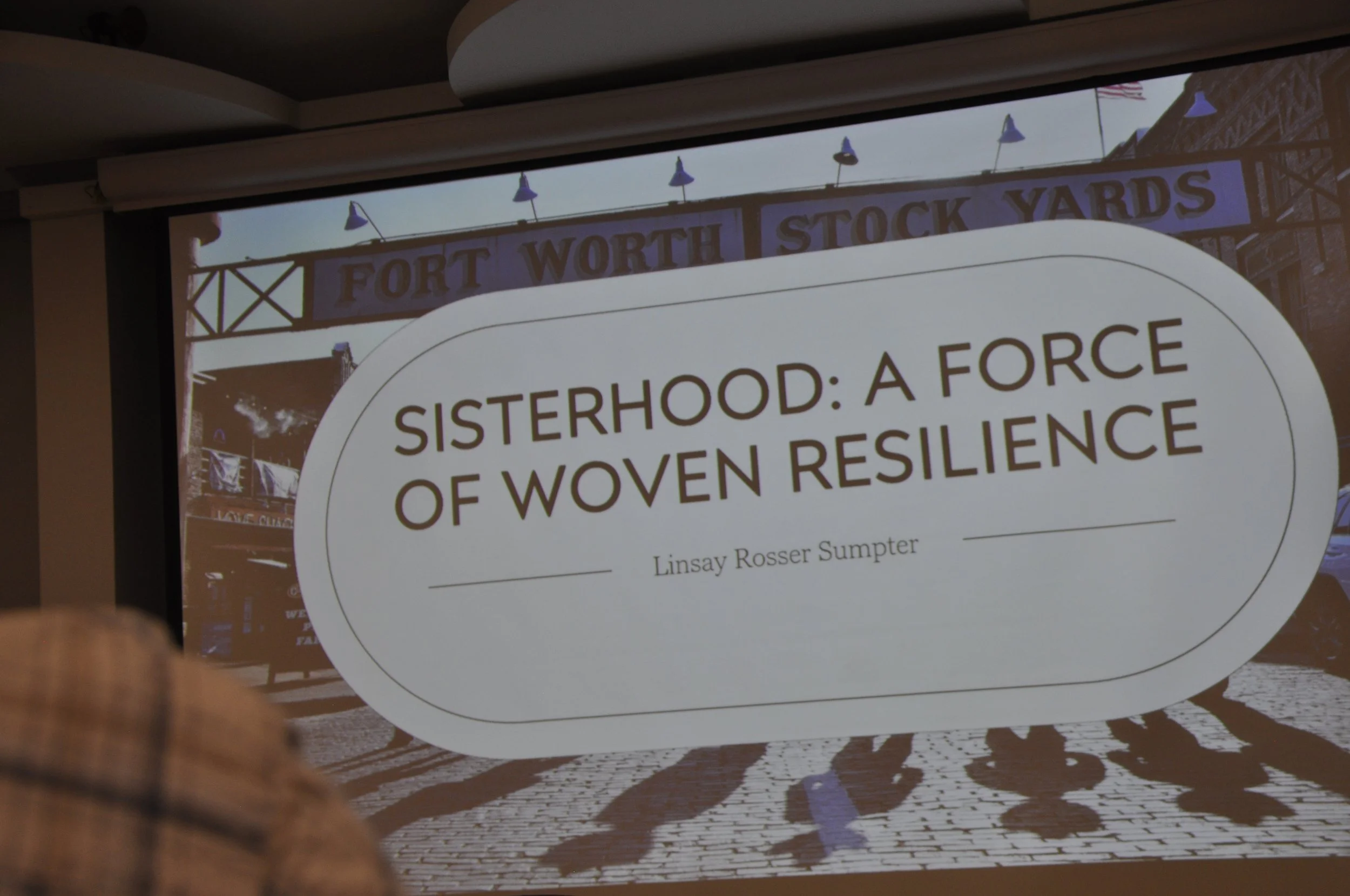 A presentation slide displaying the title 'Sisterhood: A Force of Woven Resilience' and the author's name, Linsay Rosser Sumpter, with a sign in the background reading 'Fort Worth Stock Yards'.