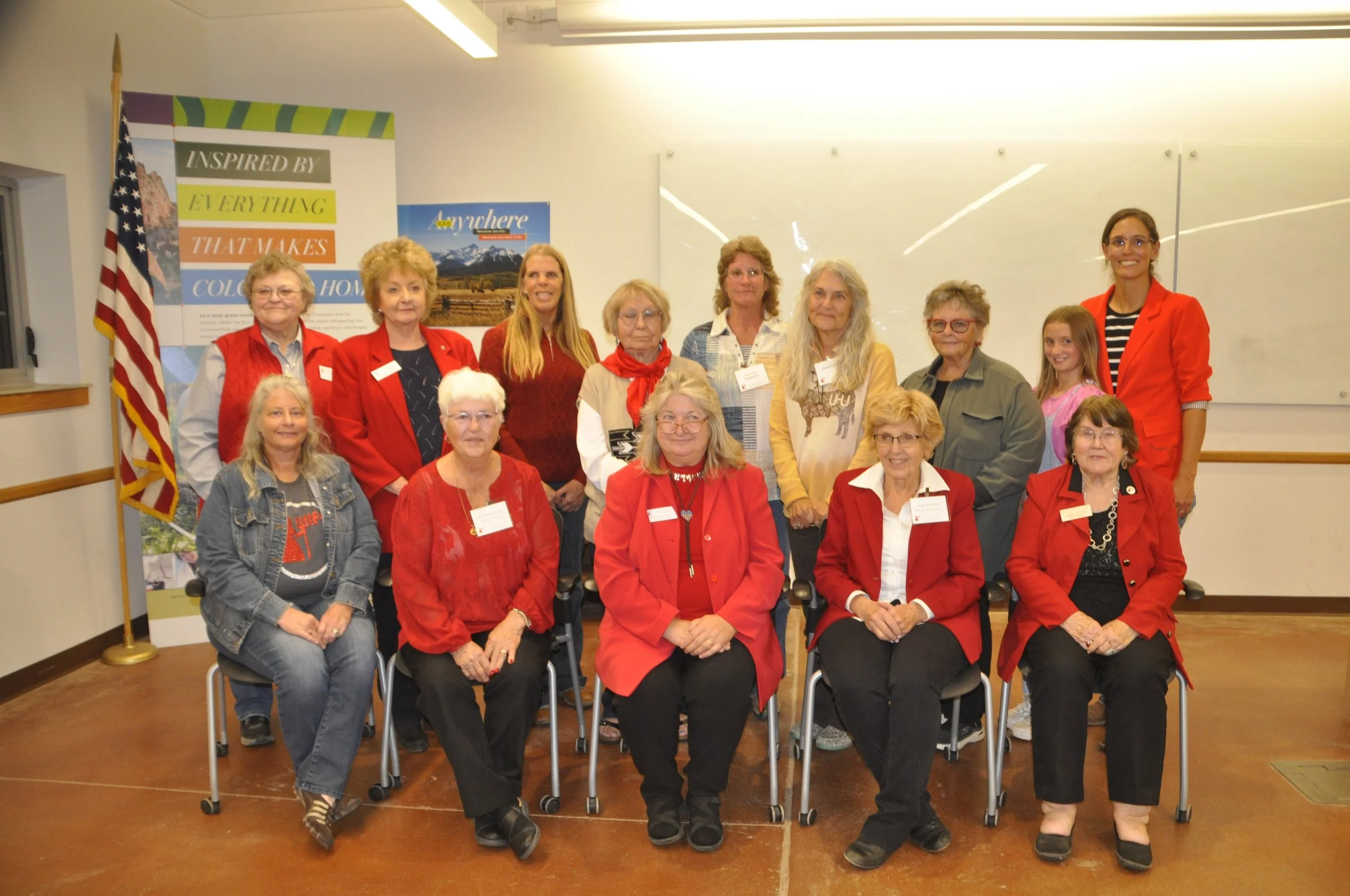 Group of women and a girl posing for a photo at an indoor event, with a banner in the background that reads 'Inspired by Everything That Makes Color Hall' and an American flag.