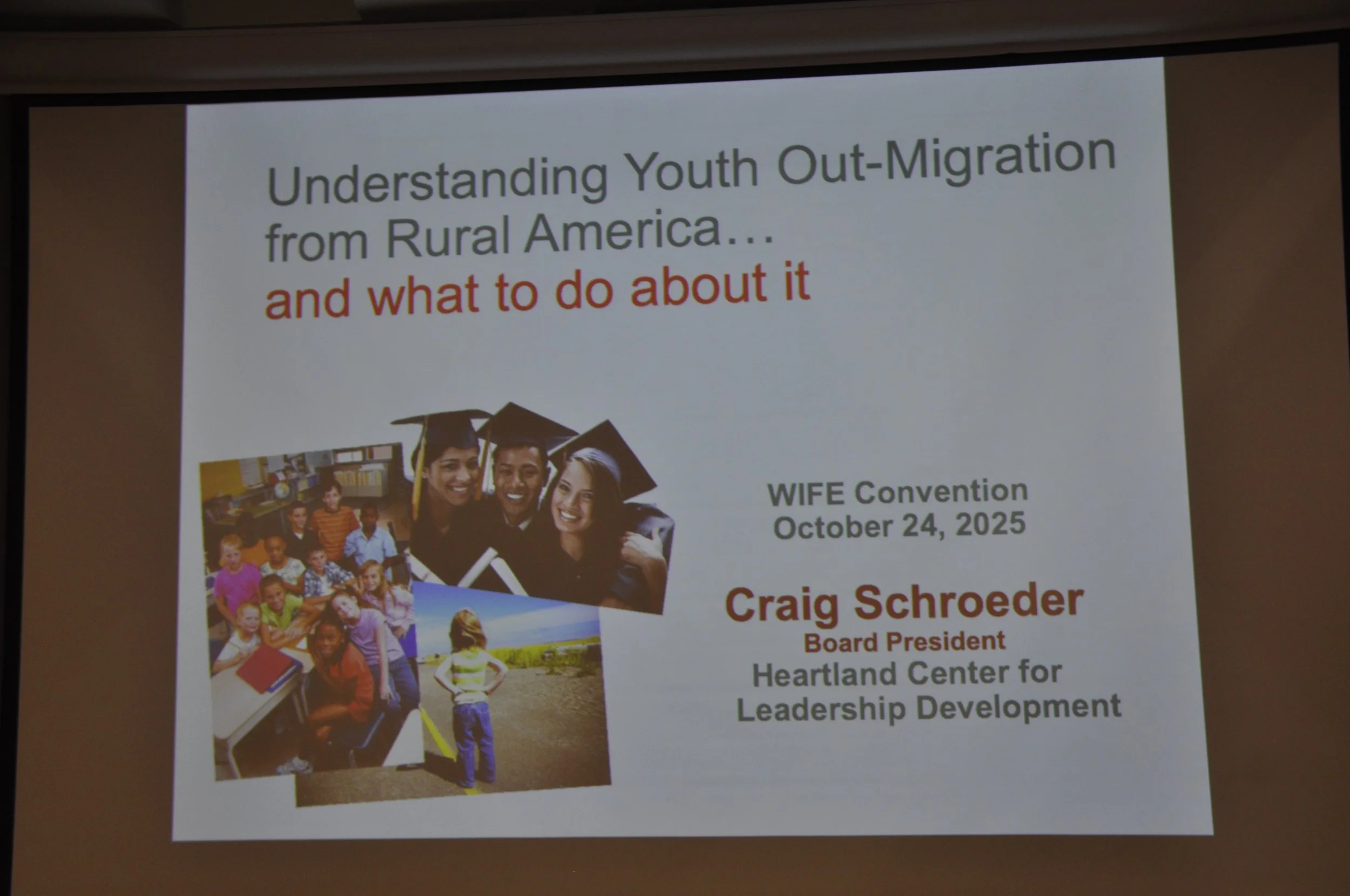 Presentation slide titled "Understanding Youth Out-Migration from Rural America... and what to do about it". It features a photo of a diverse group of young students in caps and gowns, and a smaller photo of children outdoors. The slide is part of a 