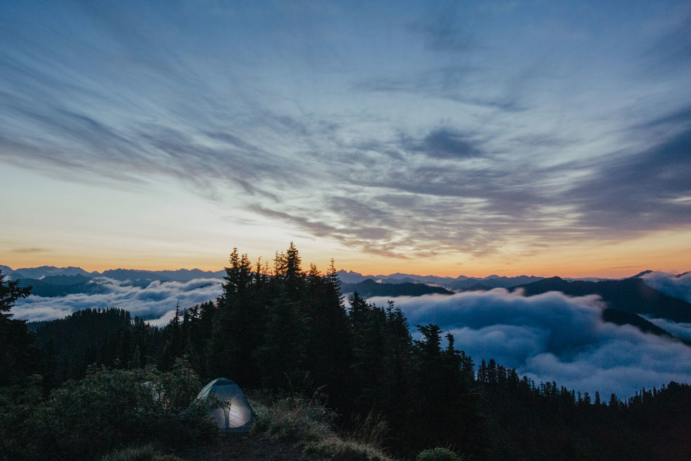 A tent, lit only by a lantern, on the top of a Washington State peak just before sunrise