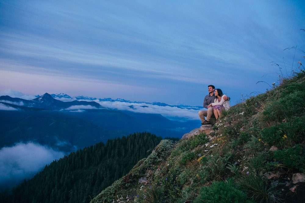 An adventurous couple snuggling on a  hill while watching the sunrise  on the top of Evergreen Mountain Lookout in Washington