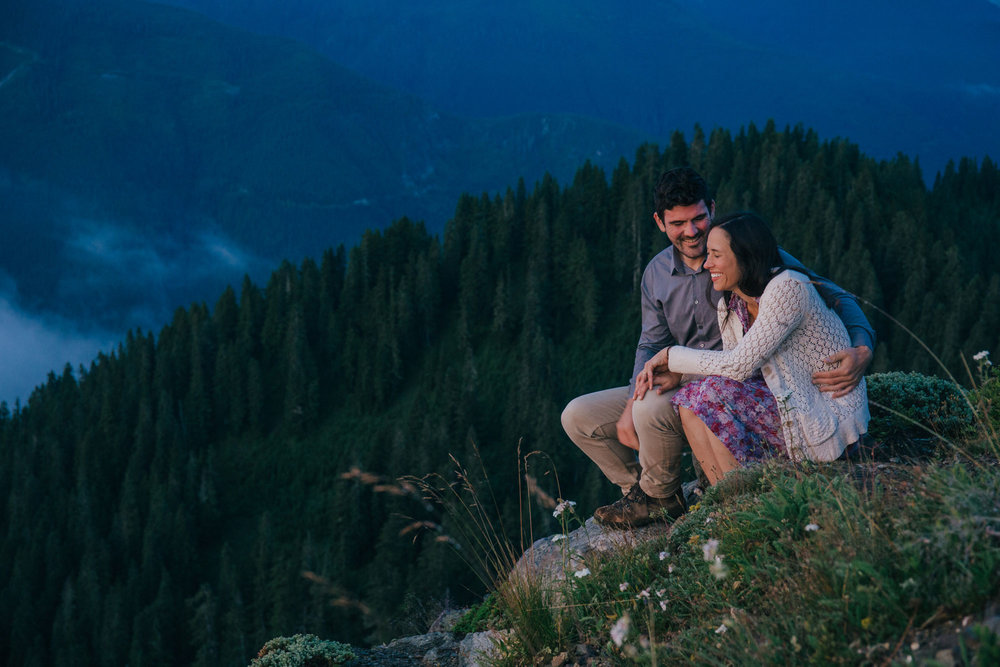 An adventurous couple sits on a hill while watching the sunrise  on the top of a Washington State Peak