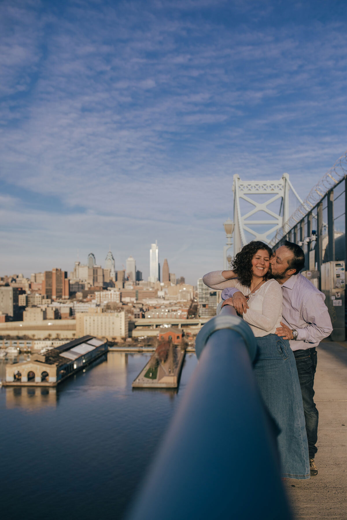 A couple snuggling on the Ben Franklin Bridge