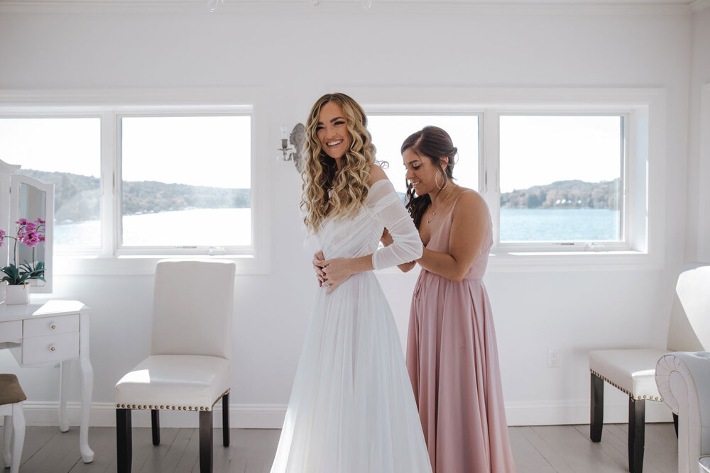 a bridesmaid helping the bride put on her dress