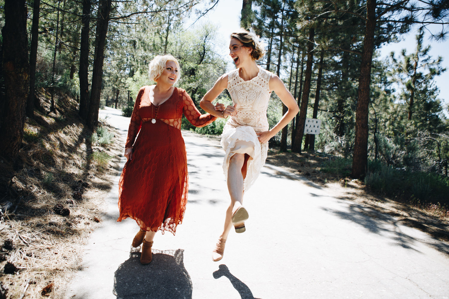a bride and her maid of honor skipping down a hill
