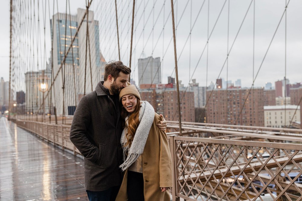 An engaged couple hugging on the Brooklyn Bridge