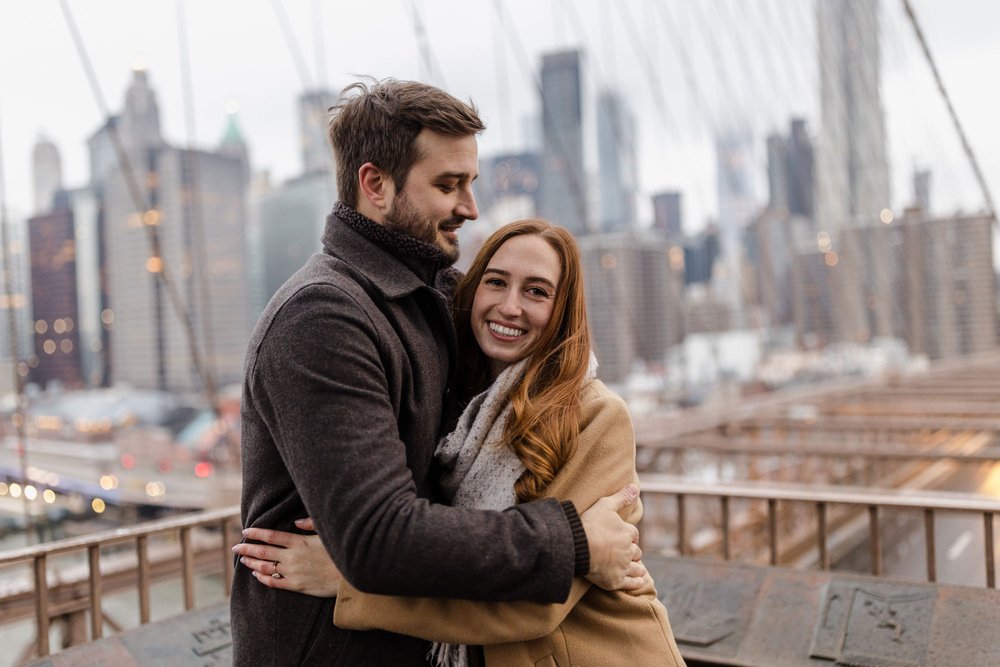 An engaged couple embracing on the Brooklyn Bridge