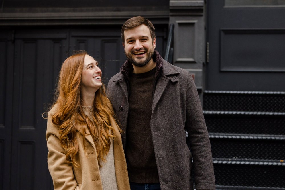 Engaged couple standing in front of a black wall in SOHO