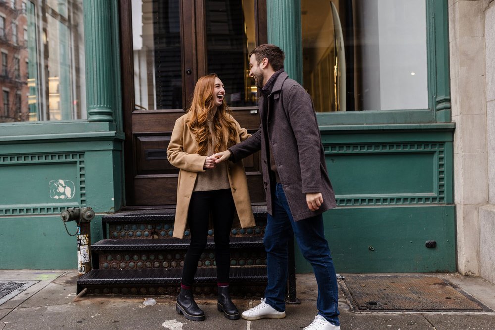An engaged couple laughing while in front of a business in SOHO New York City