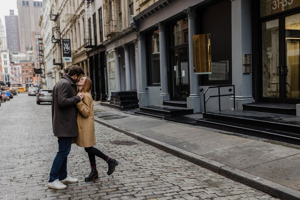An engaged couple kissing while standing on the street in SOHO in New York City