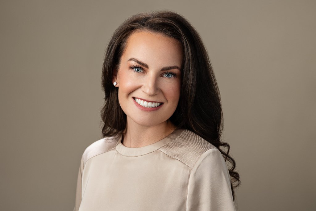 brunette woman posing for headshot in front of cream backdrop