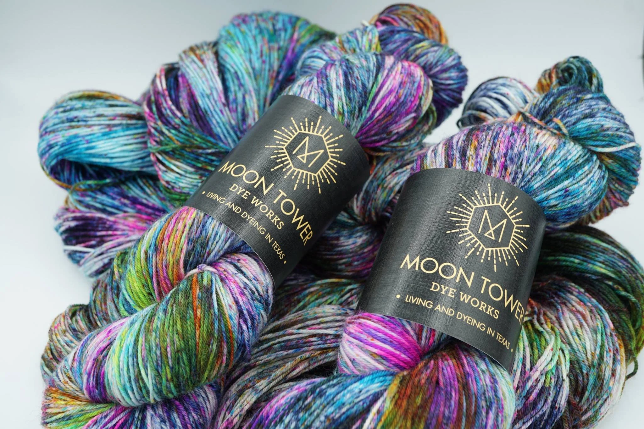 Speckled and variegated rainbow-colored yarn skeins stacked together.