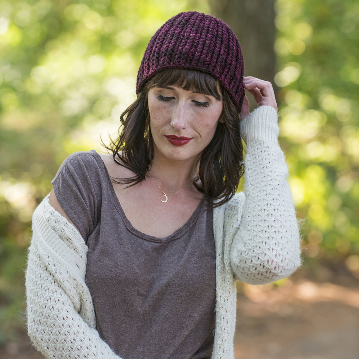  A woman in a white cardigan wearing a deep wine-colored beanie. 