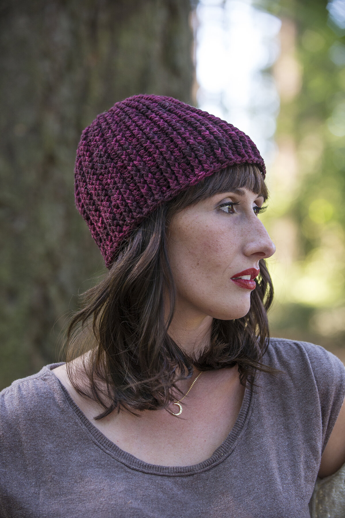  A deep, wine-colored beanie on a brunette woman viewed from the side. 