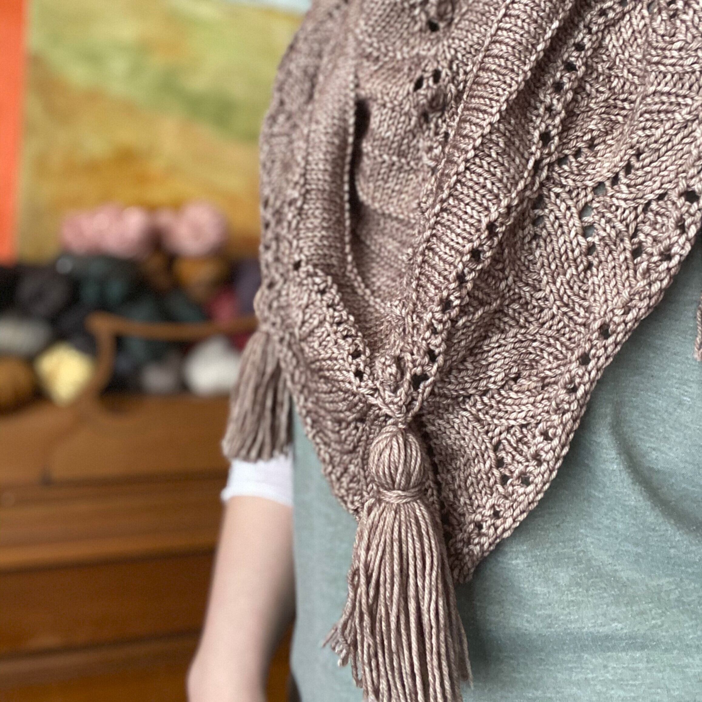 A person in a light blue shirt wearing a beige shawl with tassels.