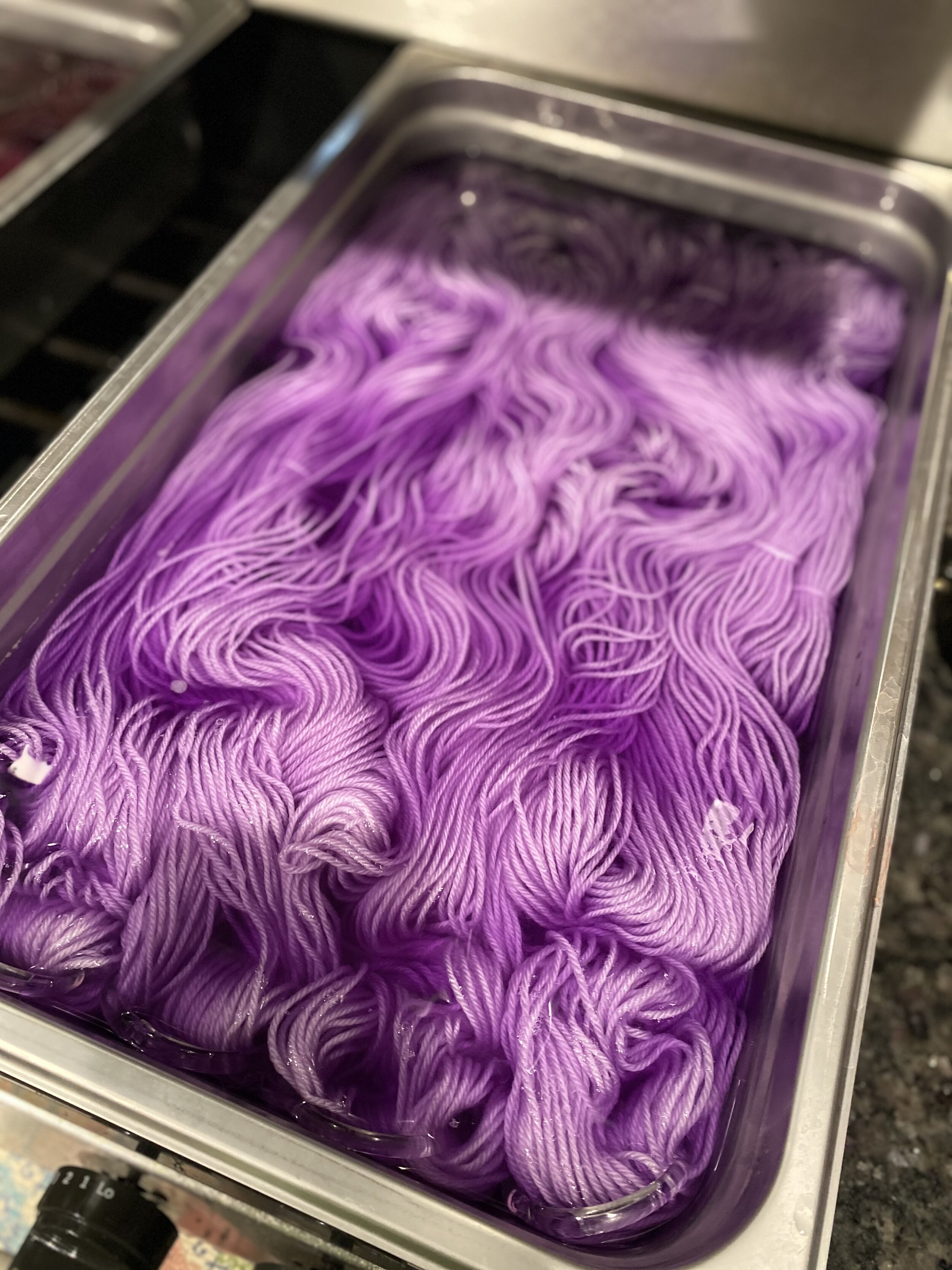 A metal pan full of yarn soaking in pink dye.