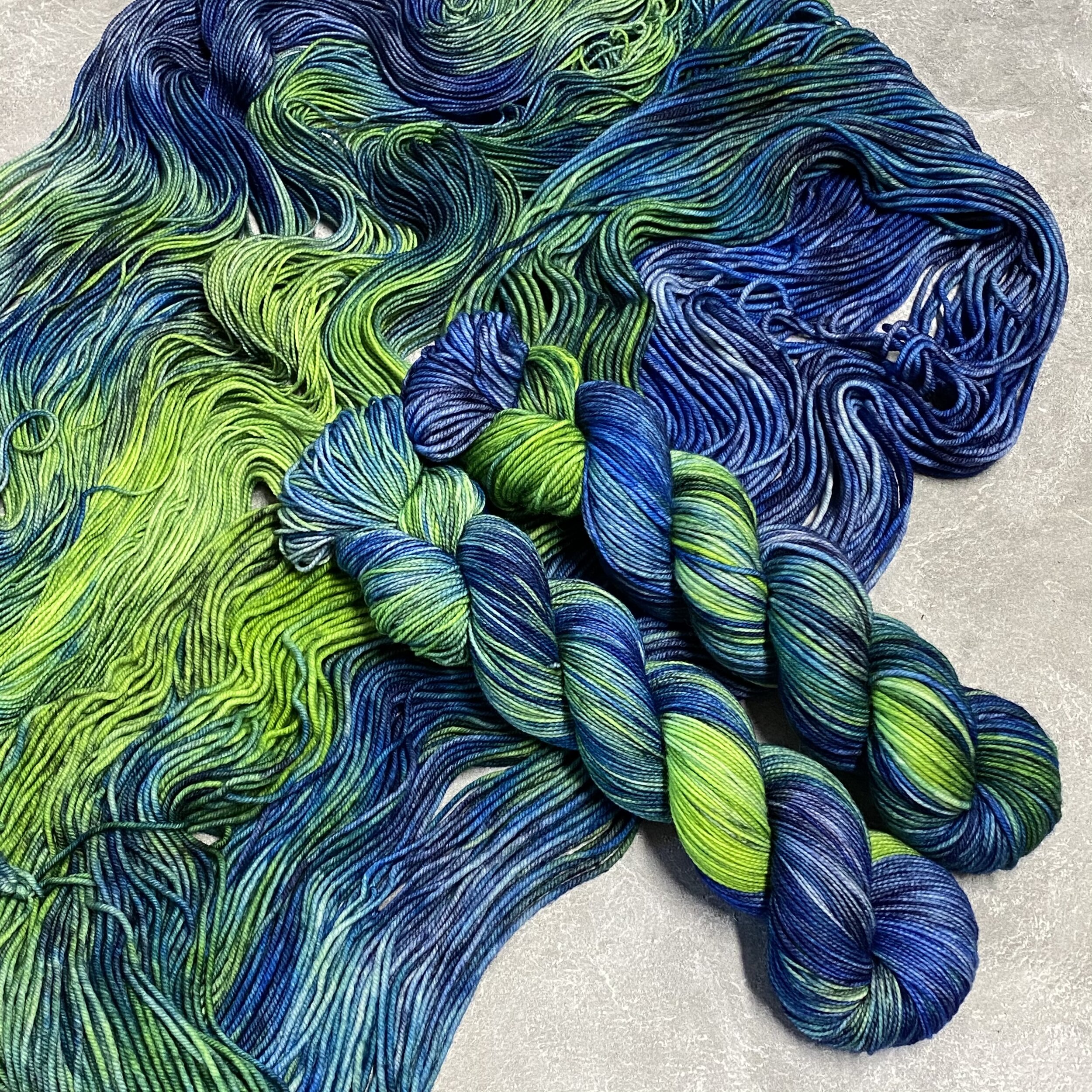 Two skeins of dark blue and lime green variegated yarn sitting on top of spread out yarn in the same color, dyed by Totally Rad Yarn.