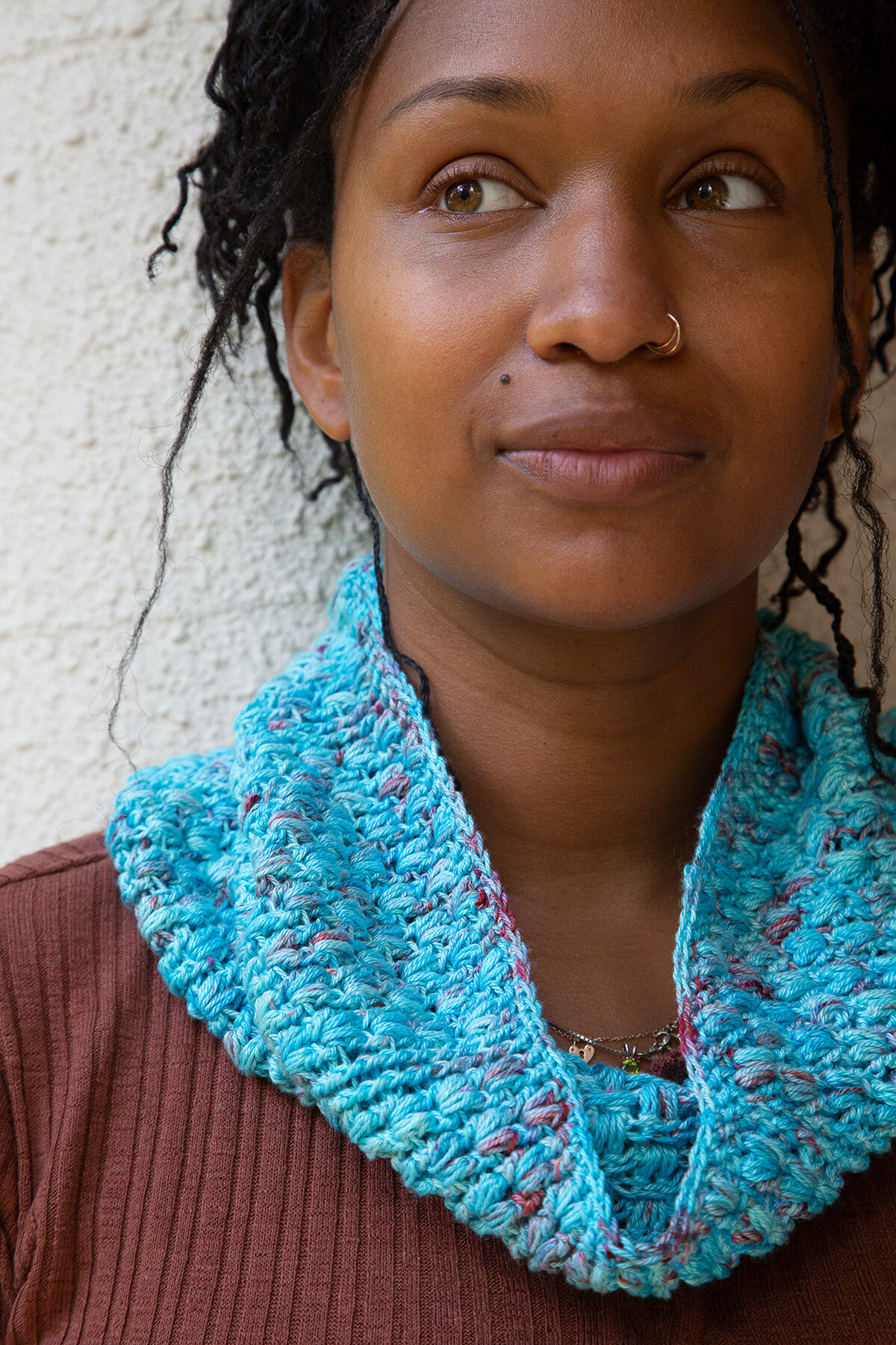 A woman looks to the side while wearing a blue crocheted Seashell Cowl.