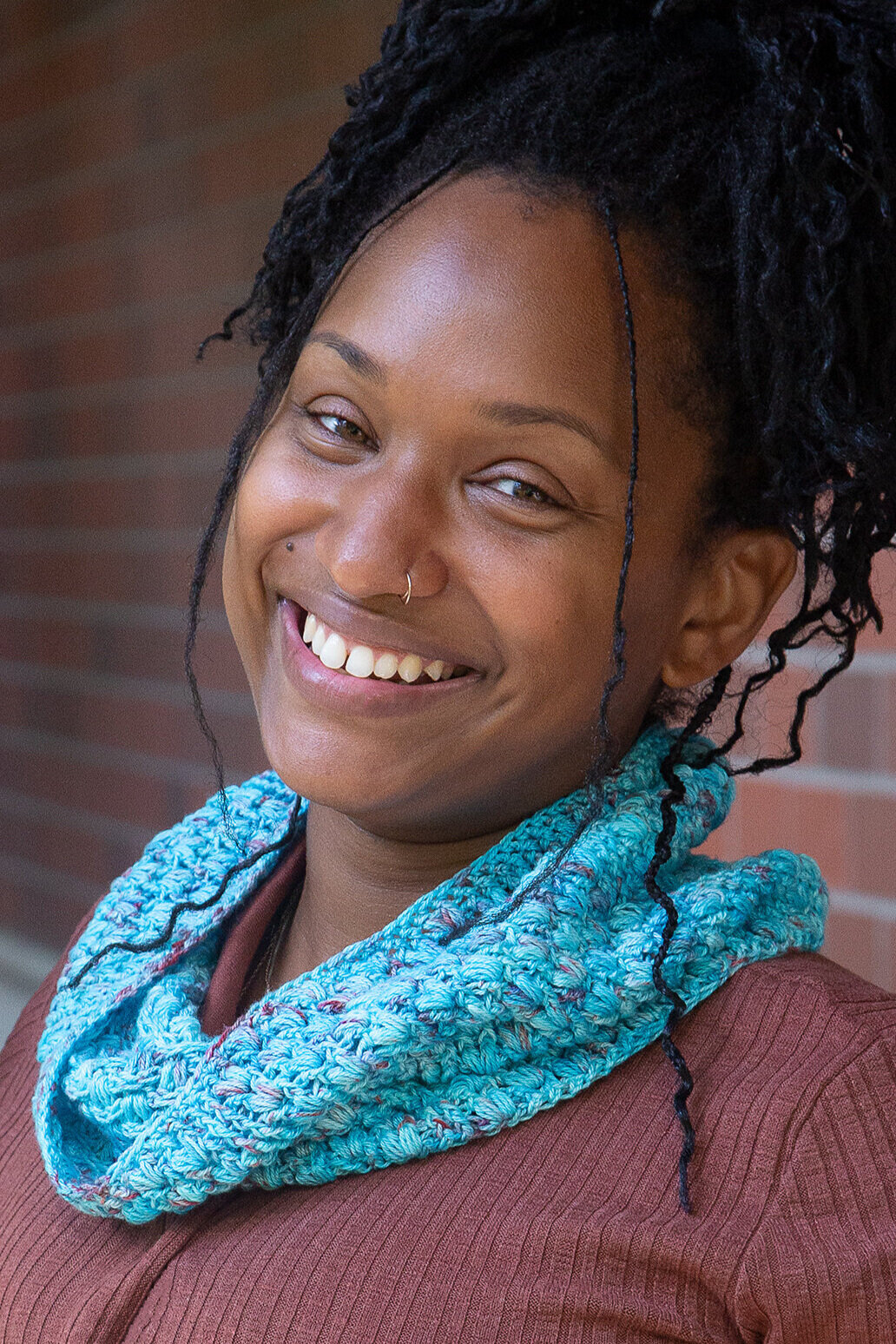 A smiling woman wears the crocheted Seashell Cowl around her neck.