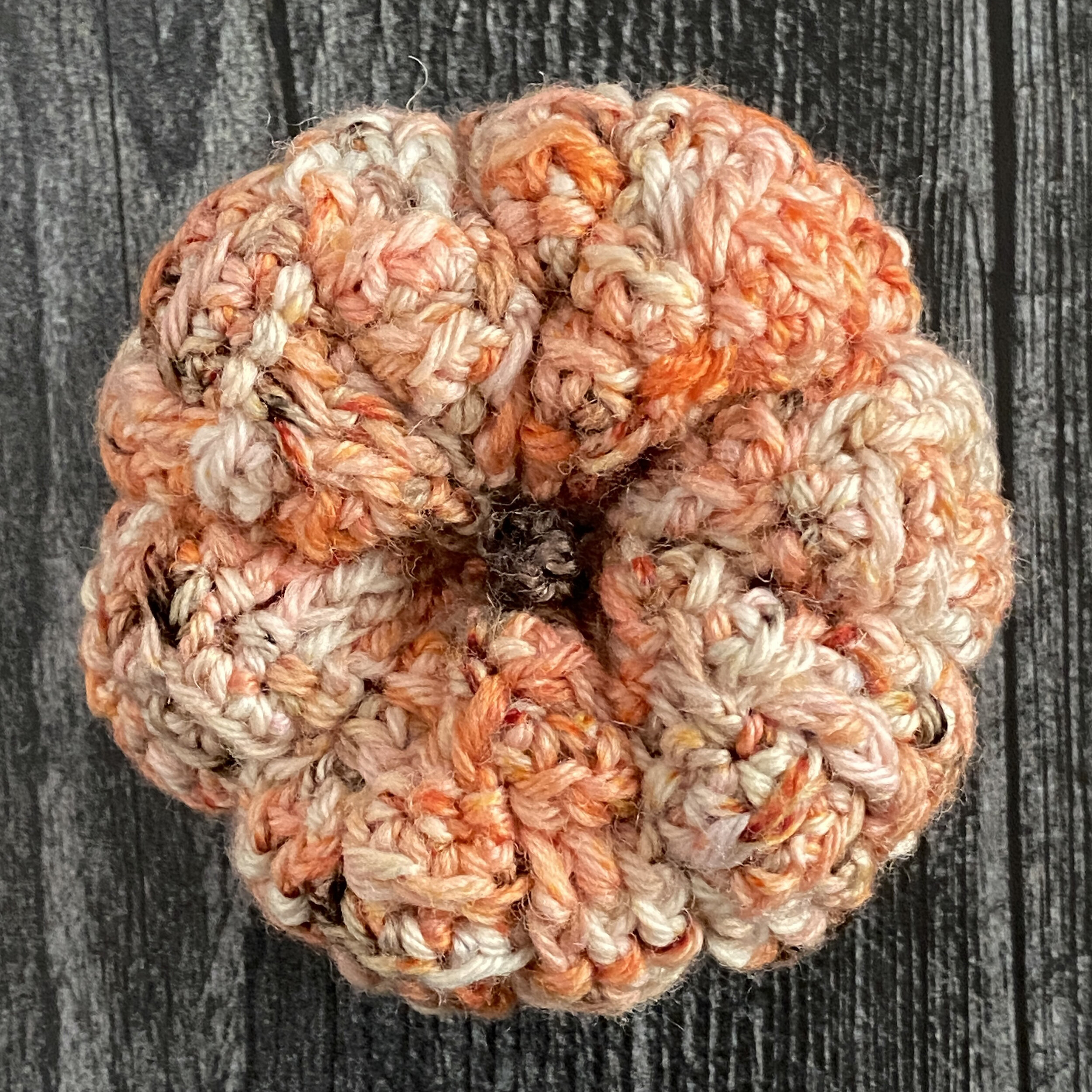 Top-down view of the crocheted Stone Path Pumpkin on top of gray wood.