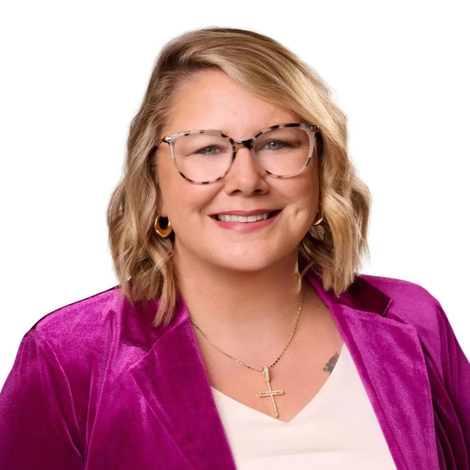 Studio headshot of a smiling woman wearing glasses and a magenta jacket against a light background in a headshot station at a Gaylord Rockies conference.