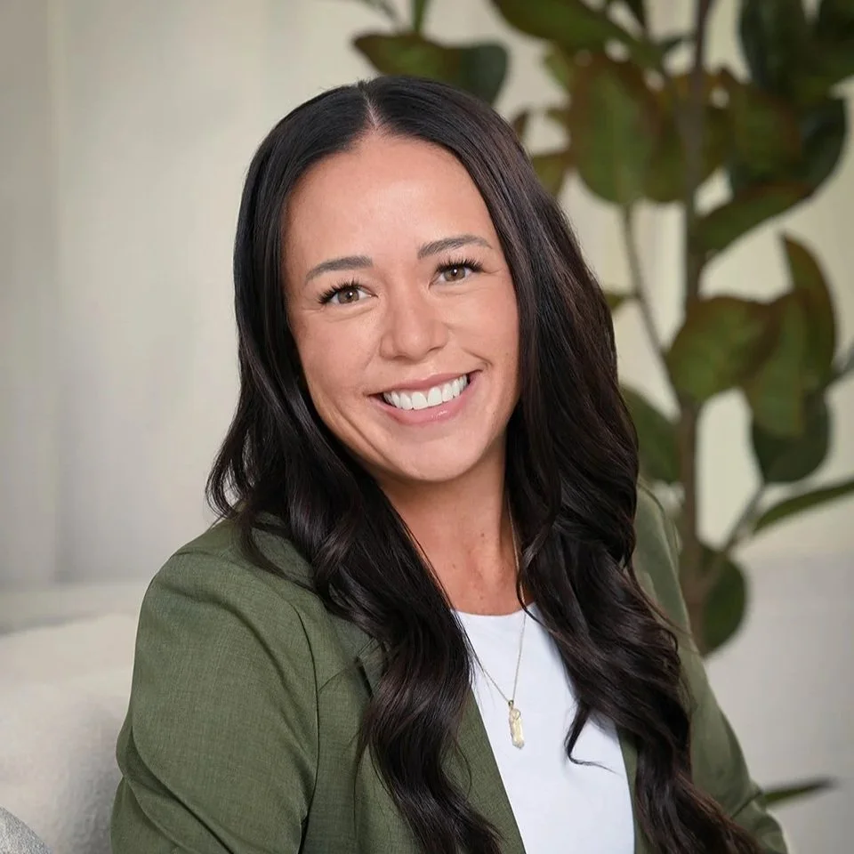 Professional portrait of a smiling woman in an olive blazer with greenery in the background, photographed by Denver Headshots.
