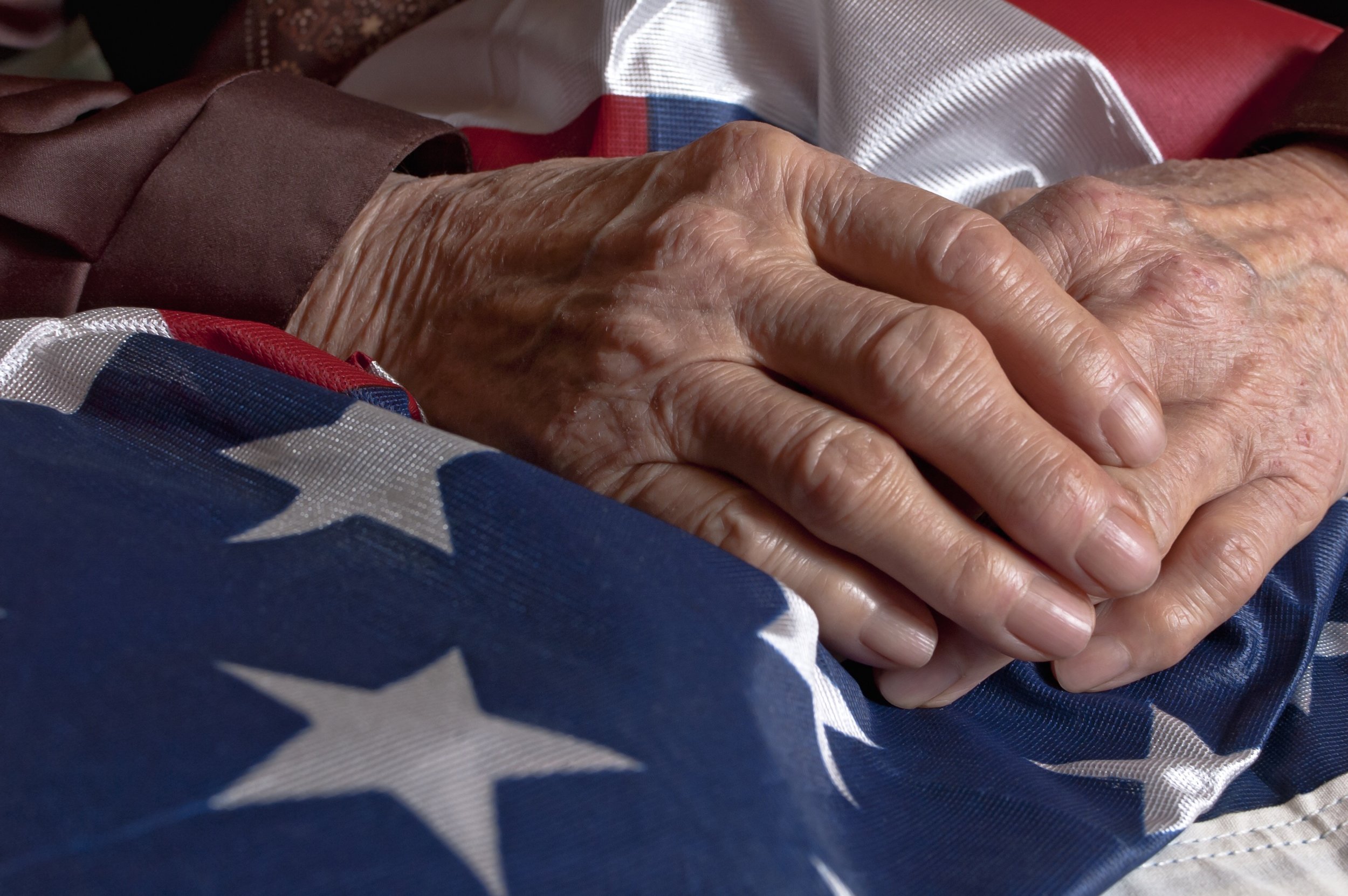 Time worn hands folded on American flag.jpg