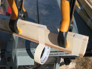 Next the wood flats are clamped together in bundles of 6. There will be some width variations, but have one edge be flush across its surface (the photo shows the bottom edge being made flush). It is helpful to select a pair of wood flats that are free of knots and place them as the outside pieces of each bundle. Later on this will keep debris from flying when these flats are ripped into tie strips. Then tightly wrap the bundles with masking tape about every 4" and remove the clamps.