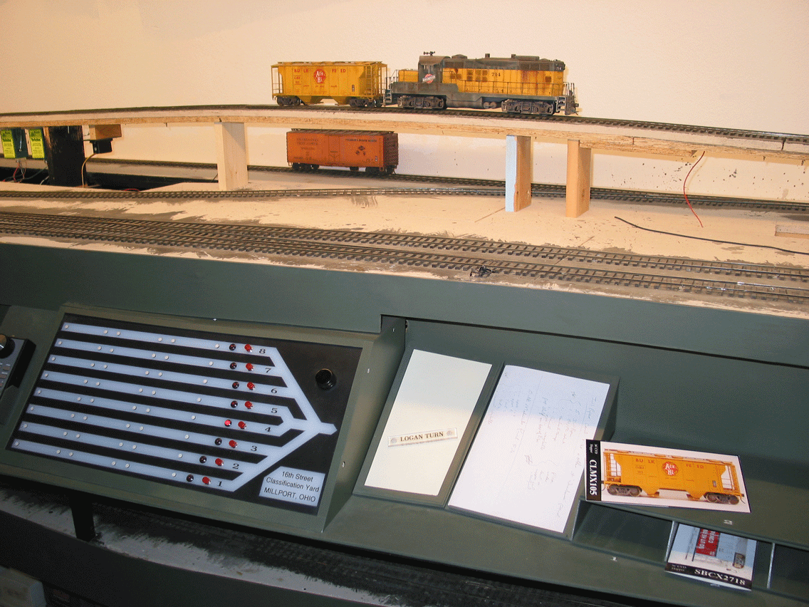 Work station for the 16th St. hump shows (left to right) panel with route selection, magnet board for "train tiles" which are placed on the panel to denote the train/track designation, a car-to-which-track list which is made up before the train is humped, and the start of card files with the car card for the one being humped laying a top the file. The CNW GP9 is by Craig Linn. 