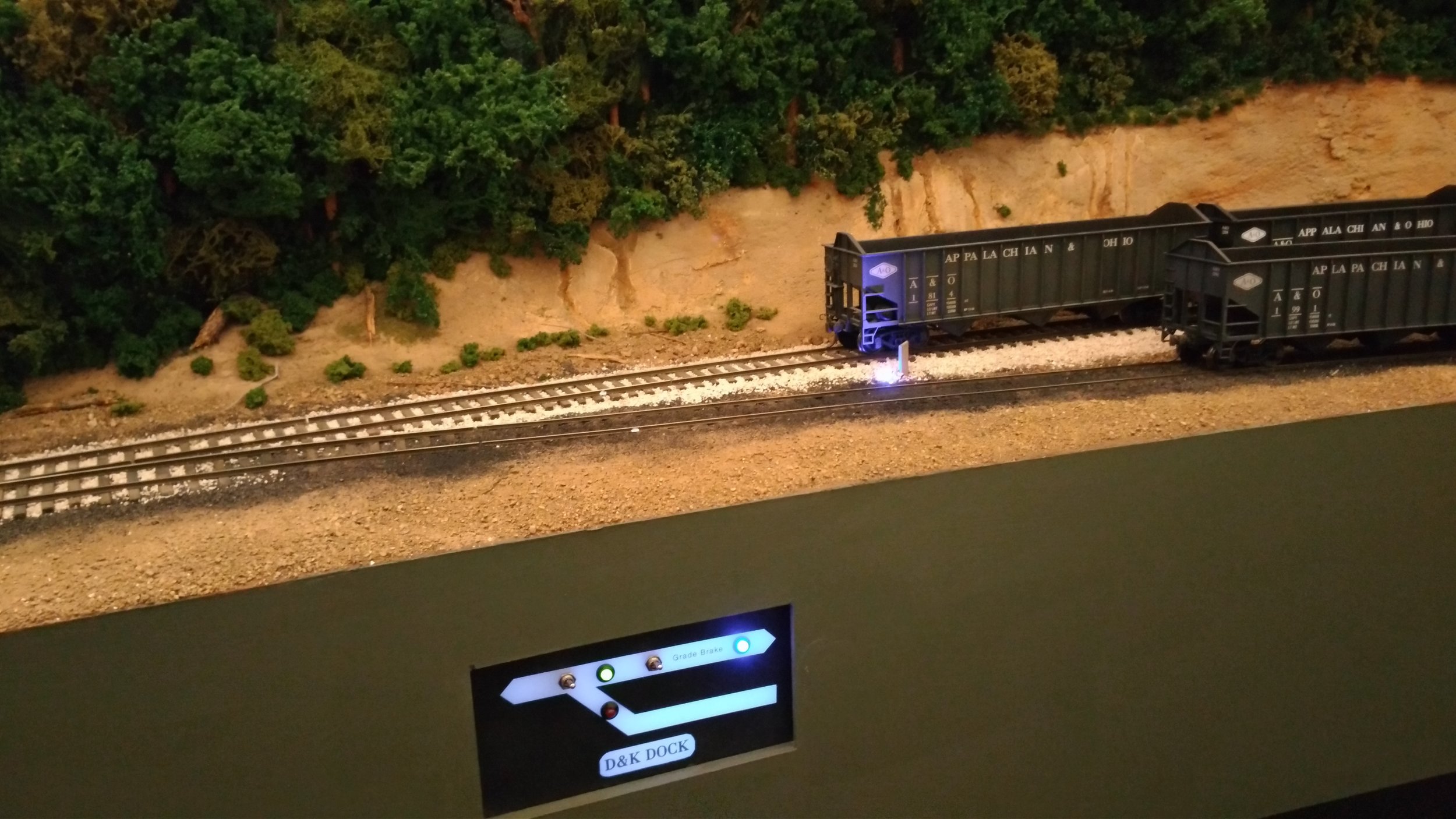  Because the main is descending a grade, the small panel includes a "Grade Brake" to hold cars while switching the dock is performed. The LED's are blue: One on the panel next to actuating toggle, and one near the track. With the ballast surround, it
