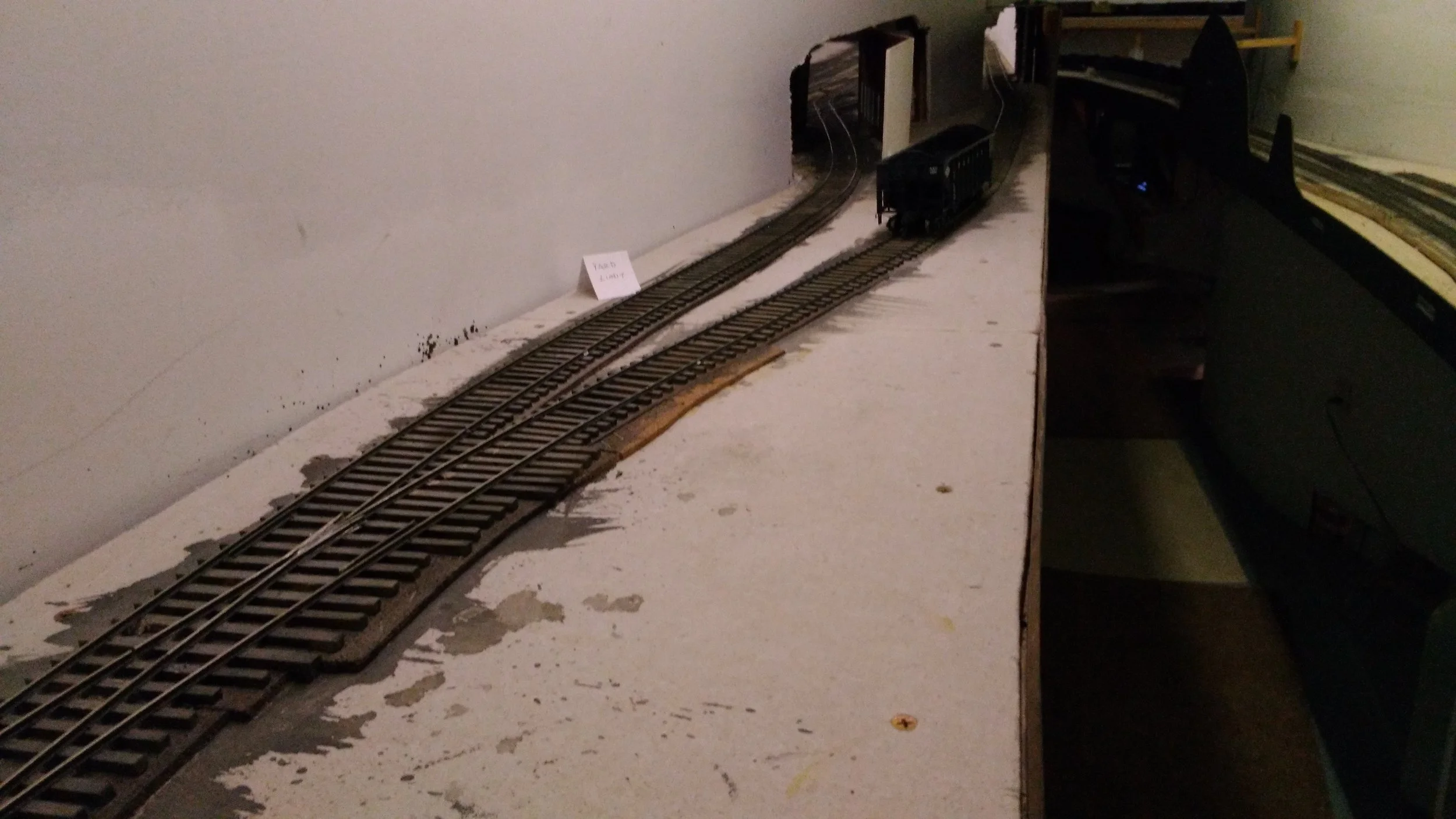 We begin a journey down the Kayford Branch by emerging from a tunnel at Apex. The Kayford main is the rear track and the portal will be about where the hopper sits. The Kayford is designed like a string of pearls....or linked sausages for a more savory metaphor.....with discreet scenes to increase the sense of isolation, and length. It is however, 150' in length, with the last town, Brooks, visible in the dim distance at the upper right; our destination.