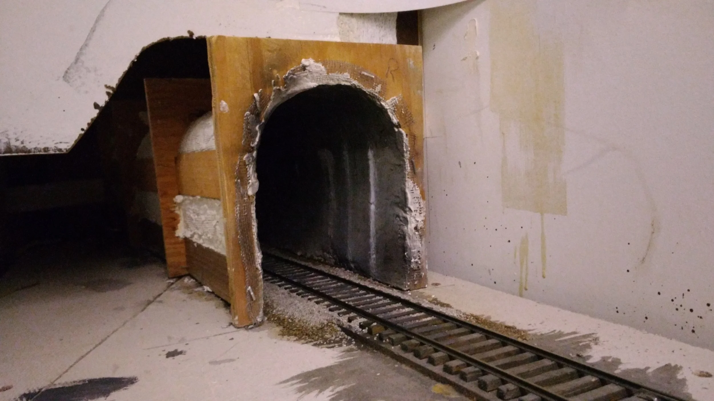 Leaving Apex we dive into Rockcut Tunnel. Lining the full length of a tunnel where possible makes sound equipped locos an awesome experience. The sound builds and the anticipation rises. The only thing missing is the hot blast. Wood tunnel formers are cut on a band saw; thin strips of wood glued to the inside (sectioned for the top piece if on a curve); screen wire stapled on; drywall mud applied; hot glued in place. Be sure to ballast the track first. :( The portal is then attached and scenery blended. See next picture for the other end!