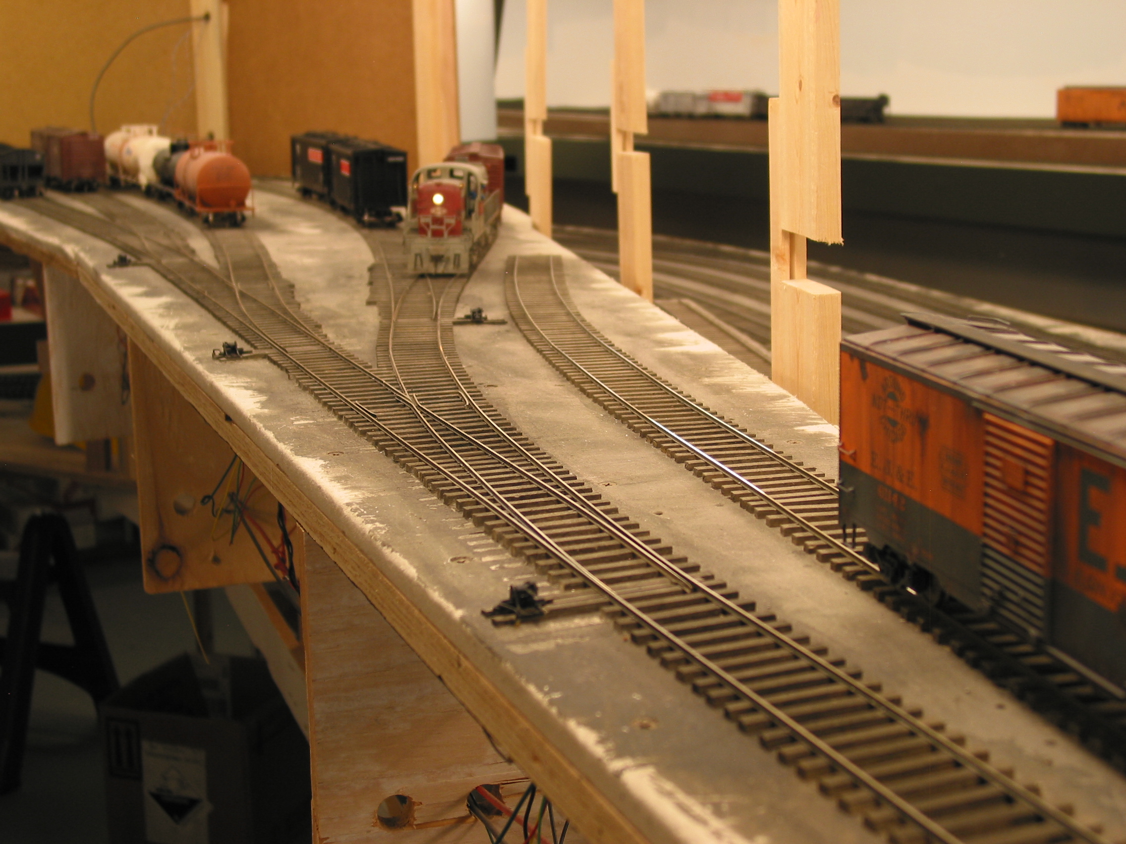  Because of the closeness of the track to the aisle, ground throws (HO) are used in Fillmore Heights. A bell crank wire actuates a micro switch underside to change polarity of the frog. The EJ&amp;E box is on the loading dock track for Firestone. 