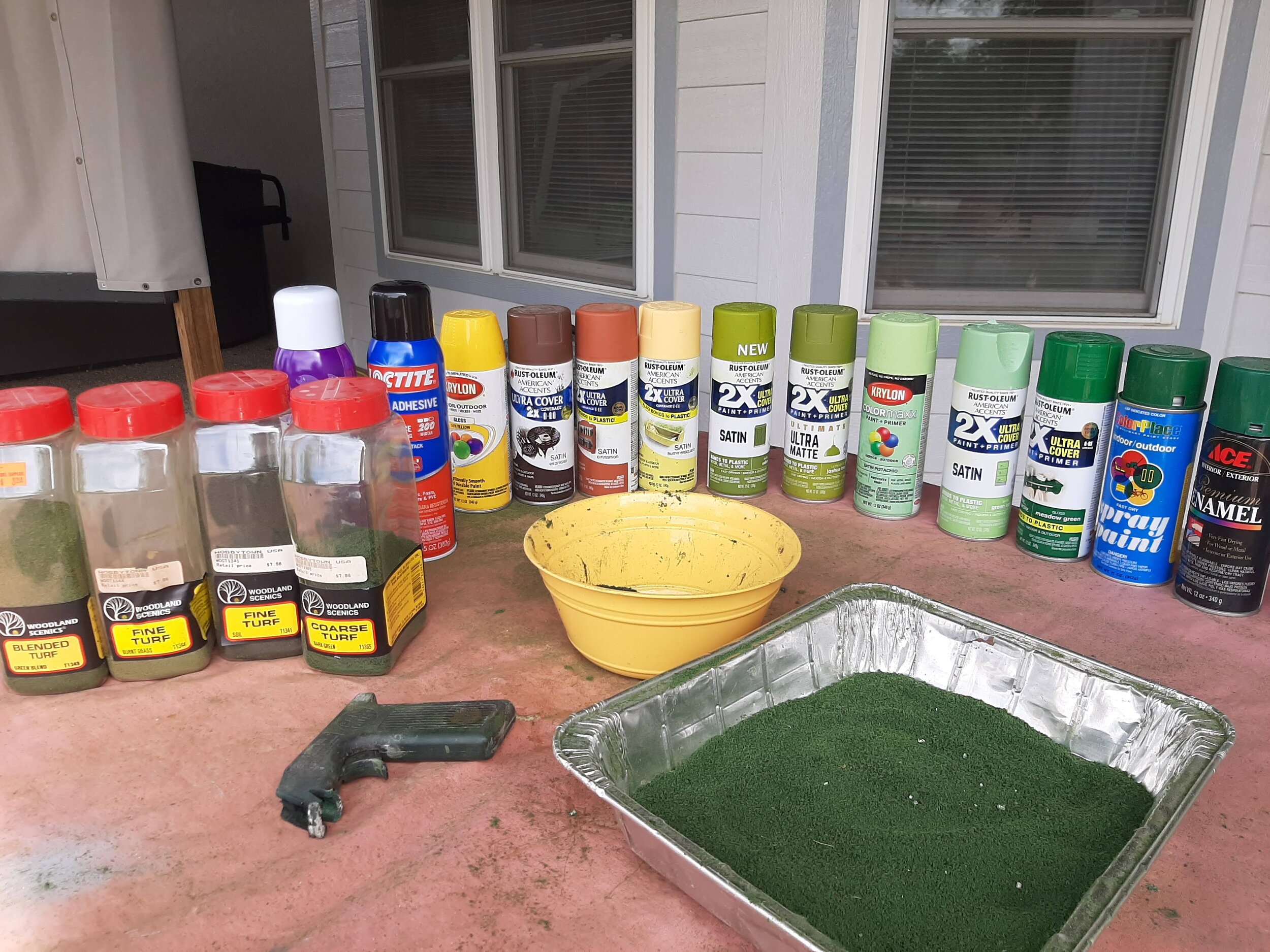  Upon an old plastic tablecloth sits the rest of the makin’s. Loctite spray glue. Cheap Superhold hair spray. A wide variety of spray paints. Woodland Scenics T65 ground foam bought in bulk. A few other colors of ground foam.   