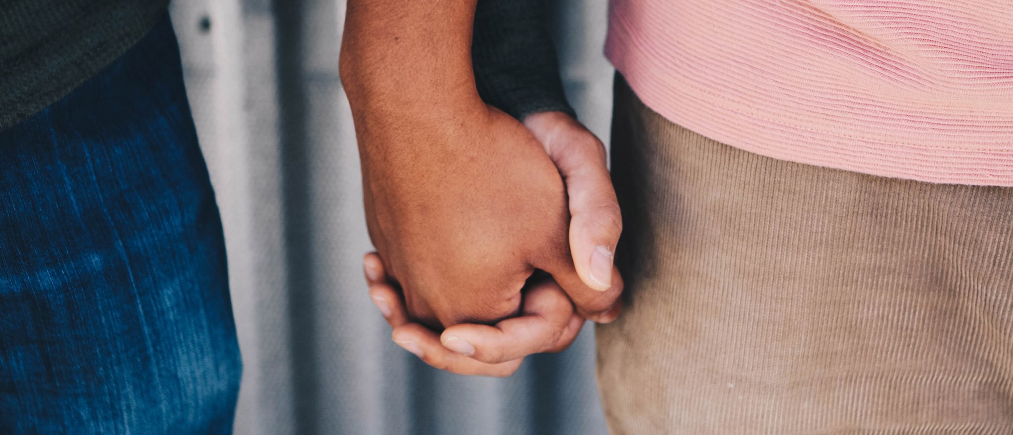 Close-up of two people holding hands, one with darker skin and the other with lighter skin.