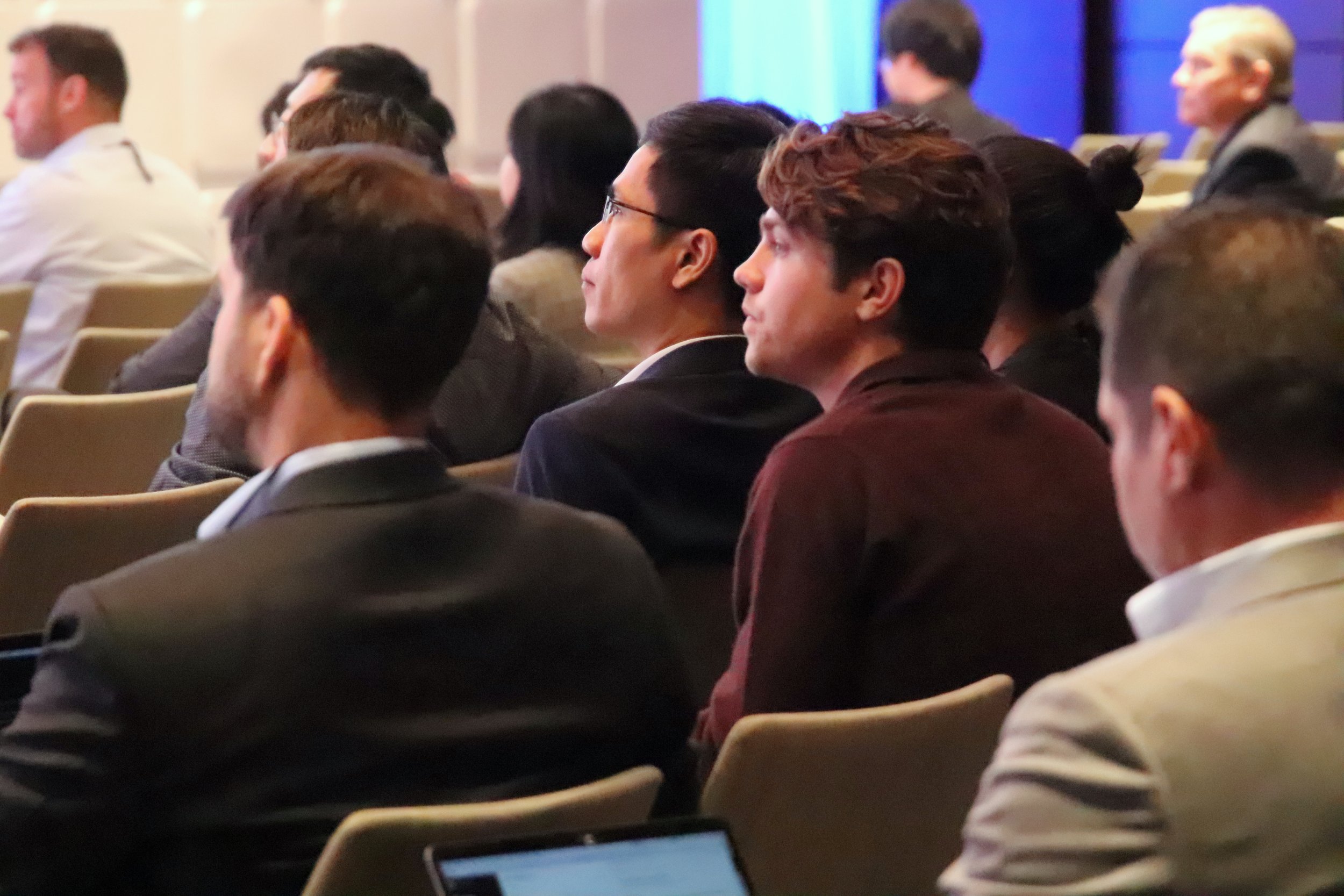 Audience members seated and attentively listening during a conference in a formal setting.