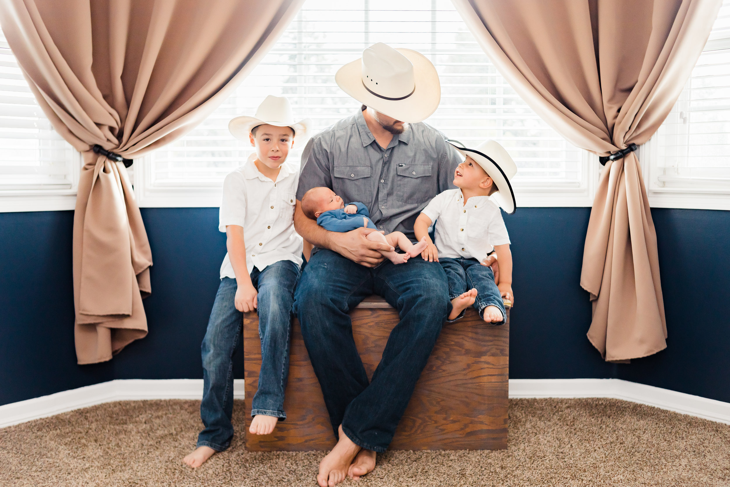 newborn lifestyle dad holding baby with brothers wearing cowboy hats