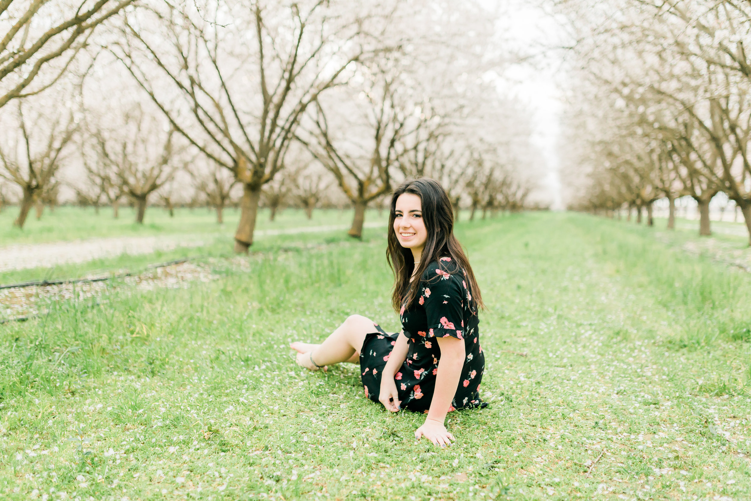 senior girl sitting on grass in a blooming orchard