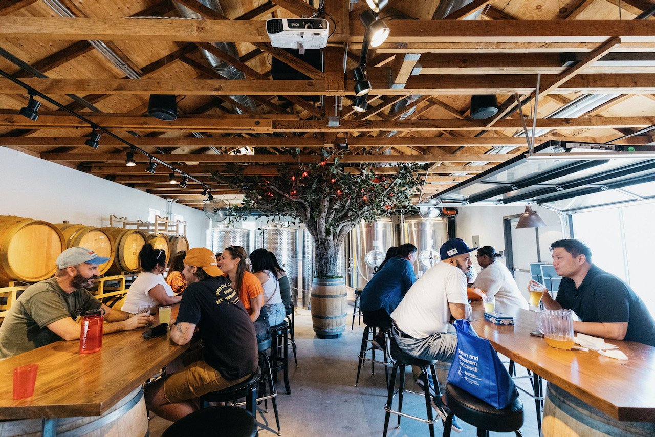 A full cider house with people sitting around the two long tables