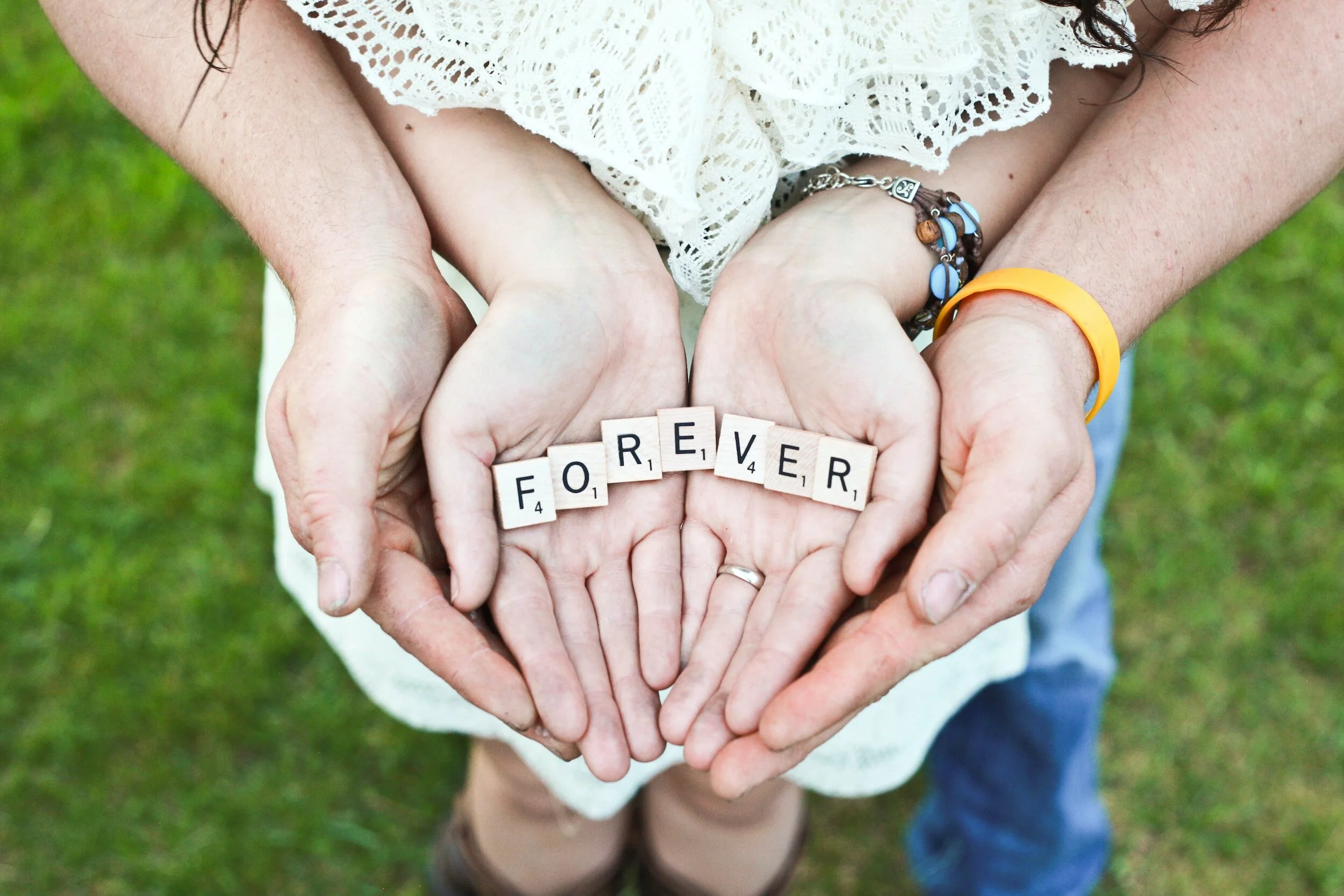 Image of man and wife's hands holding scrabble letters that spell "forever: