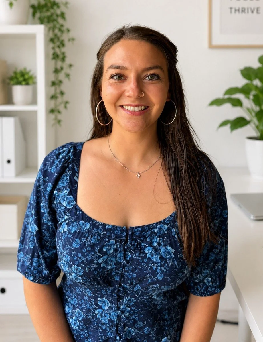 A woman with long brown, wet hair, smiling, wearing hoop earrings, a small nose ring, and a silver cross necklace, in a bright modern office with white shelves, plants, and a framed motivational poster.